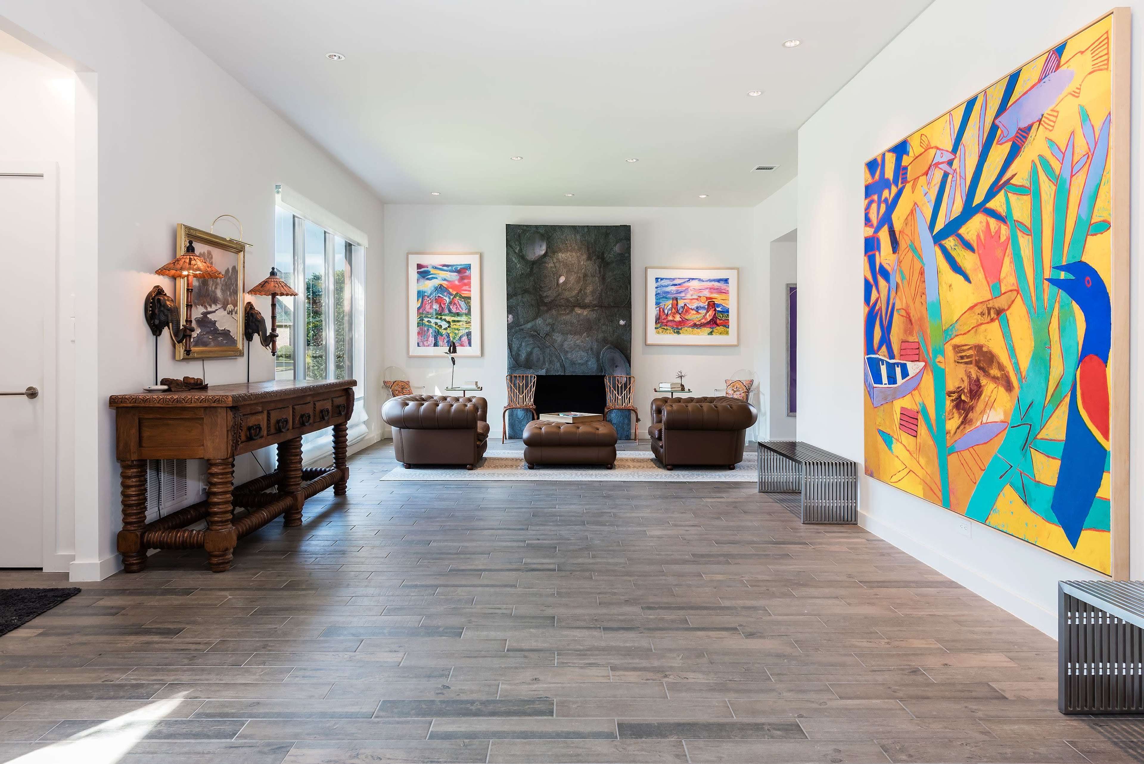 A bright living room featuring modern artwork on the walls, a fireplace, and brown leather sofas arranged around a central rug.