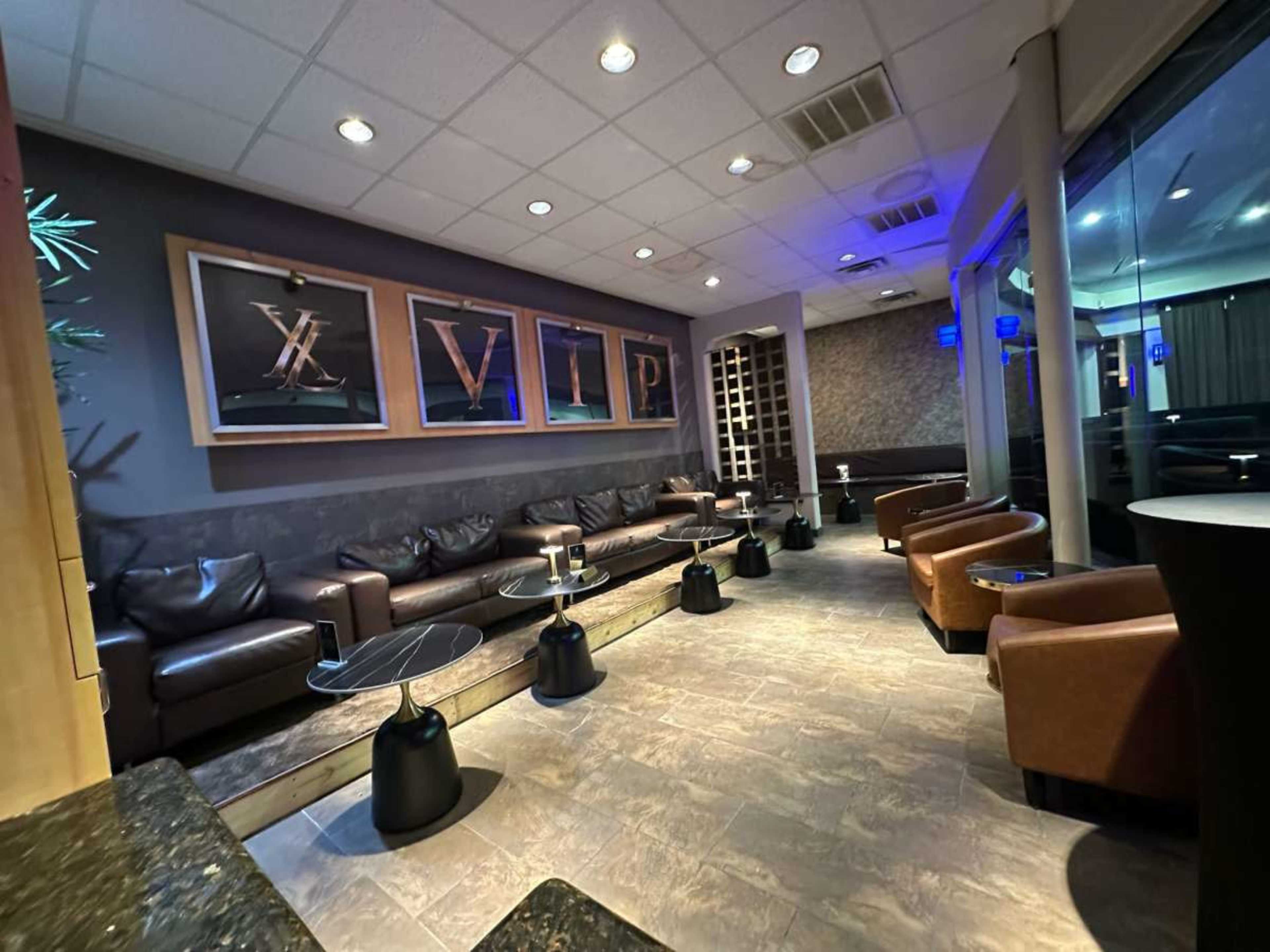 The image shows a modern lounge area with brown leather seating, small tables, and framed artwork on the walls.