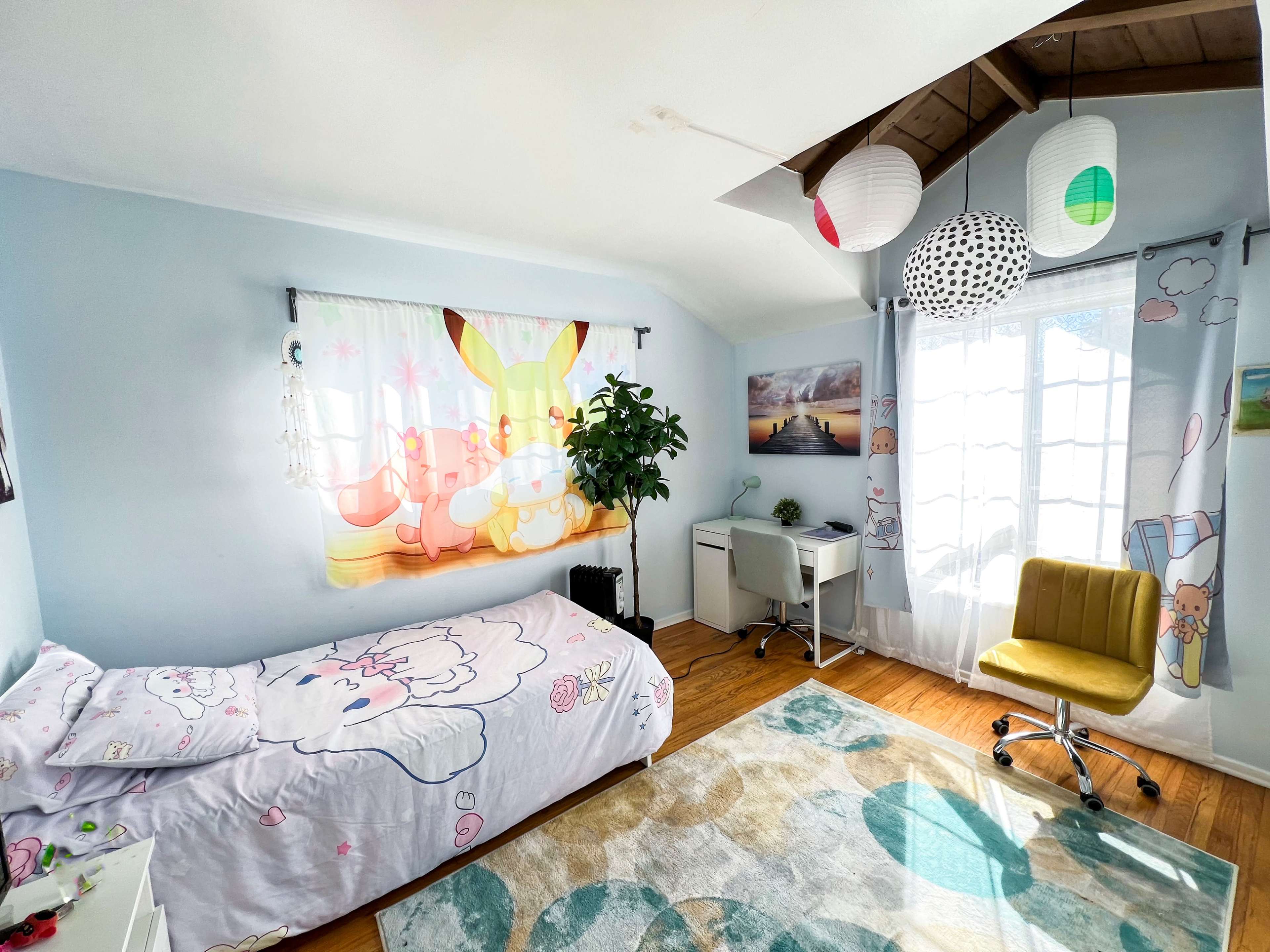 The image shows a brightly decorated bedroom with a bed featuring a playful bedspread, a desk and chair in one corner, and a window adorned with colorful paper lanterns.