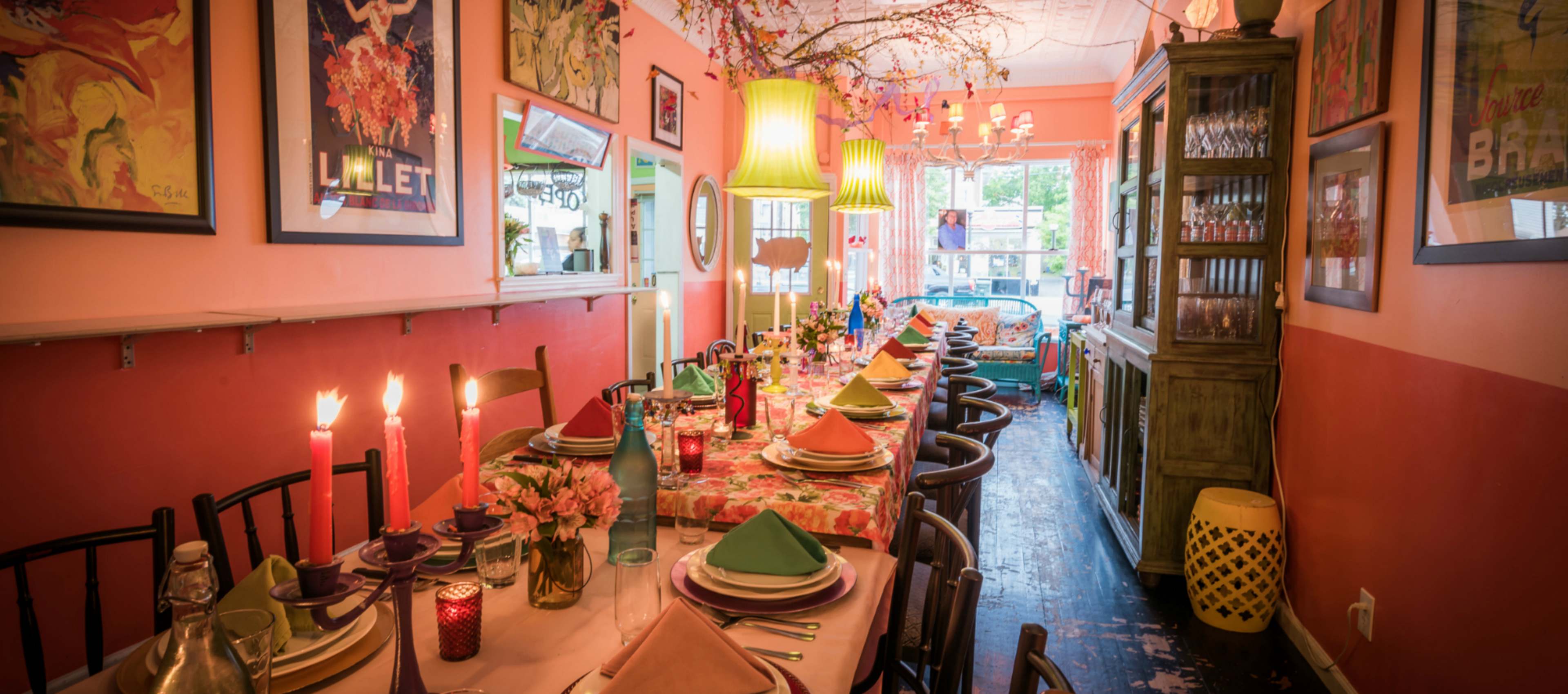 The image shows a warmly decorated dining room with a long table set for a meal, featuring vibrant tableware and floral centerpieces.