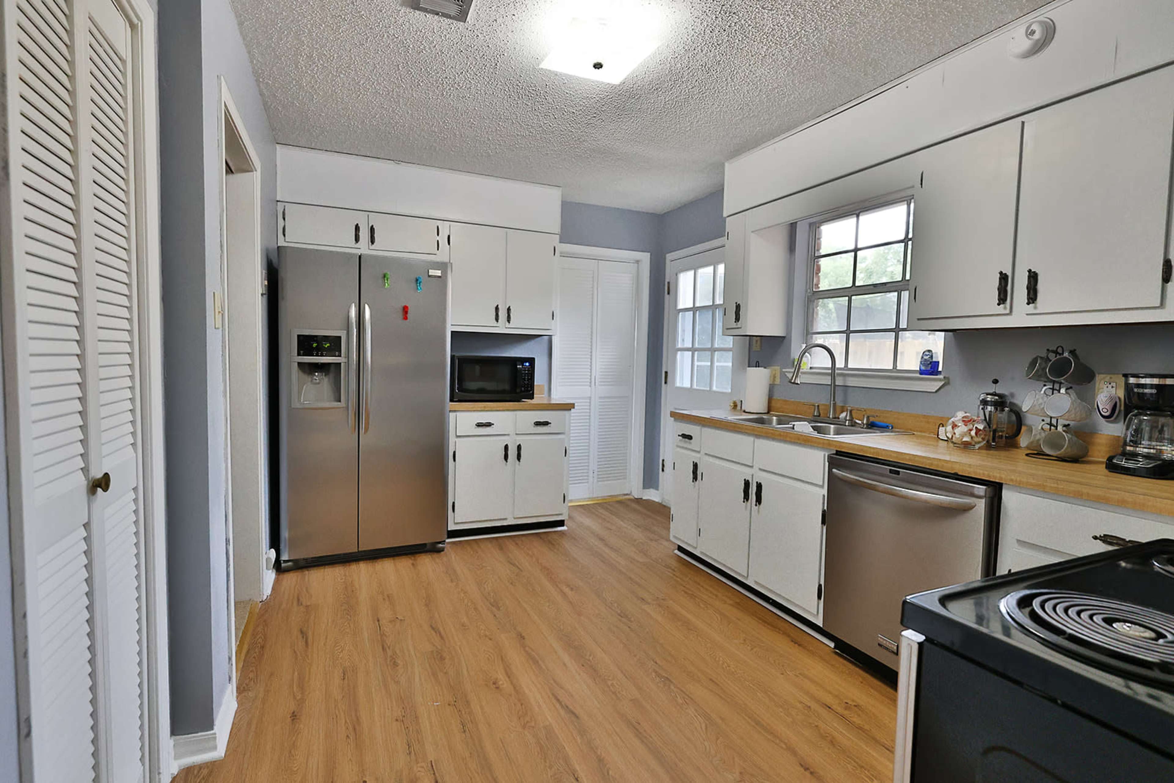 A kitchen with stainless steel appliances, white cabinets, and a wood countertop, featuring a window and a door leading to an outdoor area.