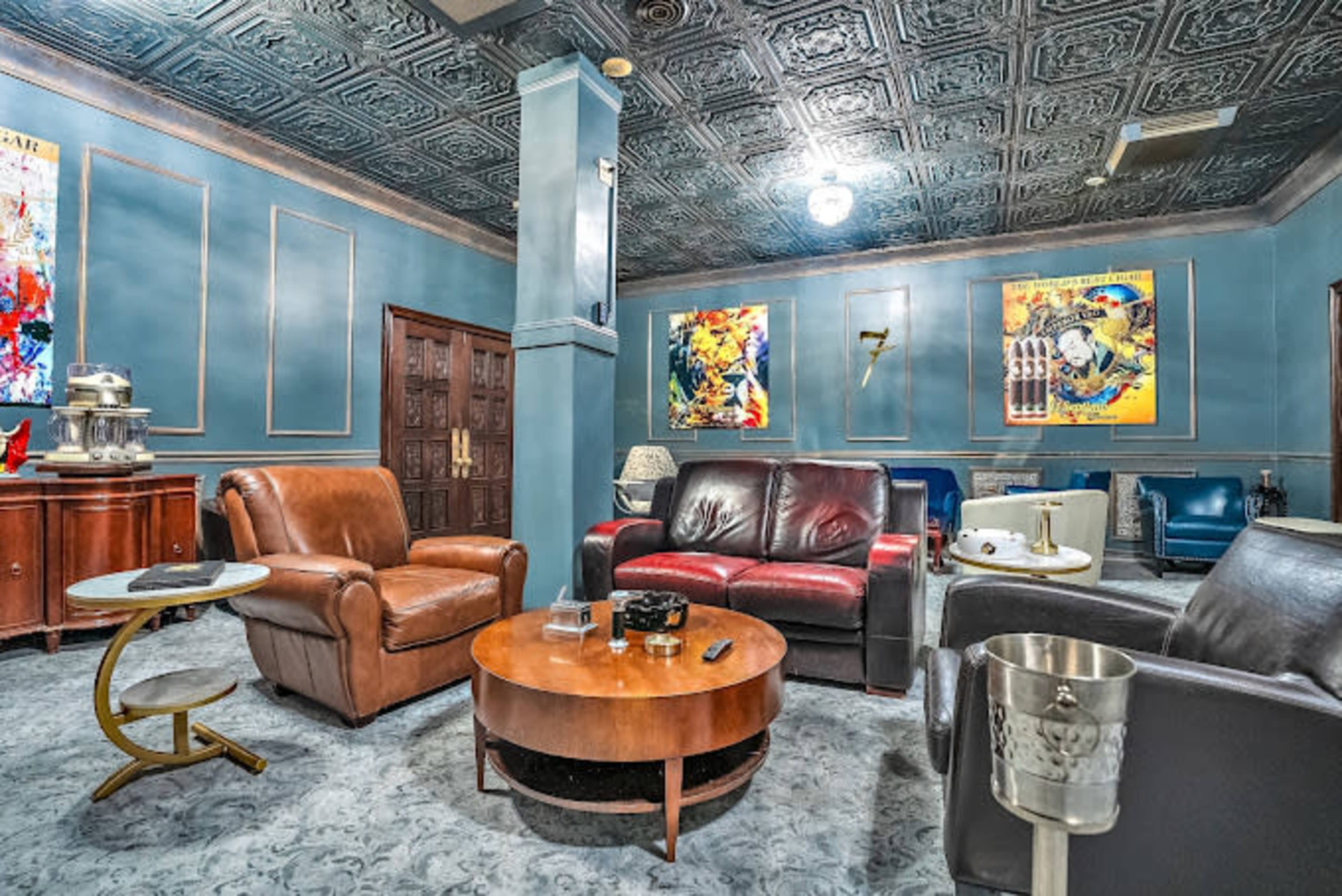 The image shows a vintage-style lounge area with leather seating, a round wooden coffee table, and colorful artwork on the walls.