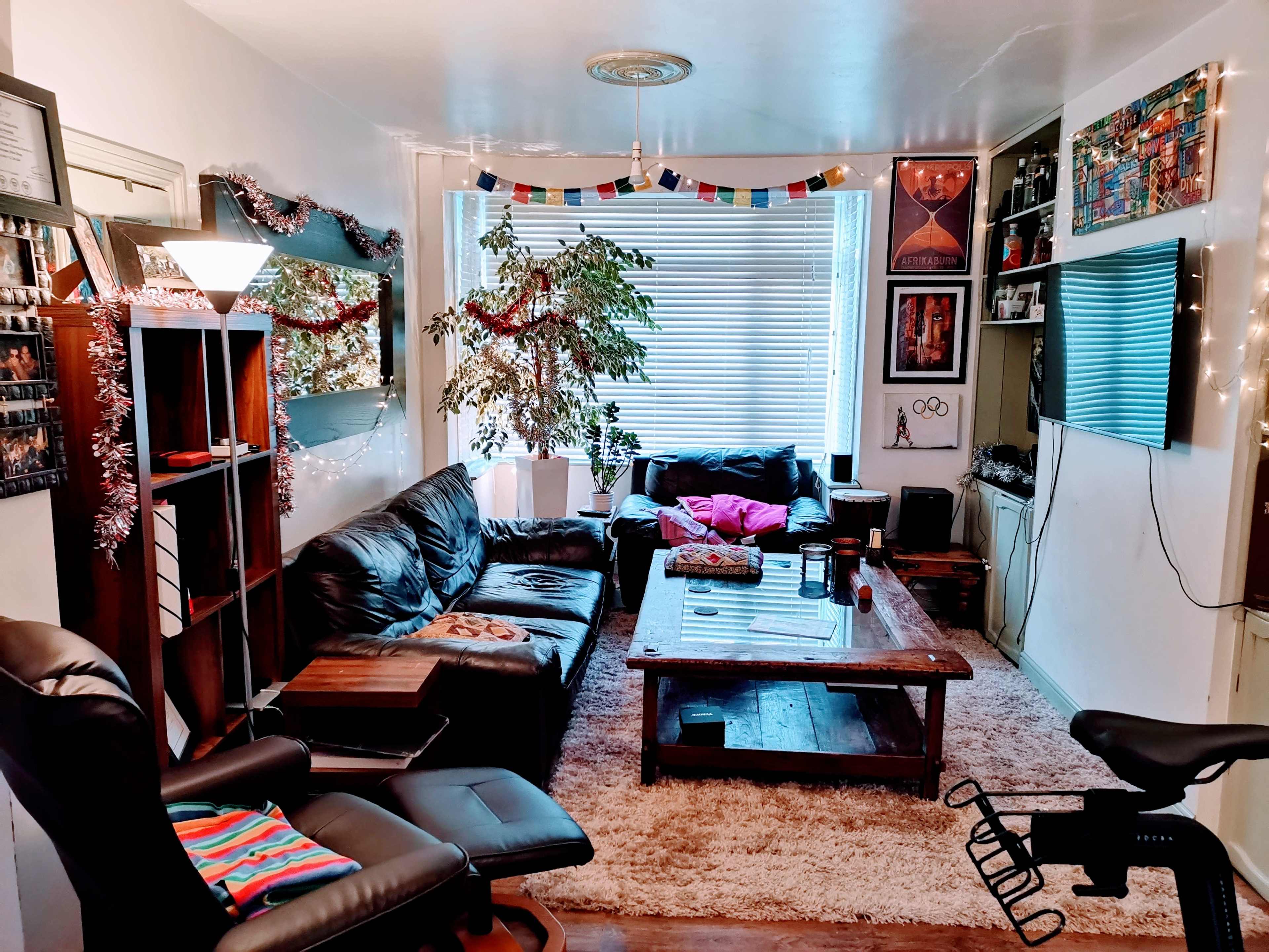 The living room features a black leather sofa, a wooden coffee table, and shelves lined with artwork and decorations, with natural light filtering through the window.