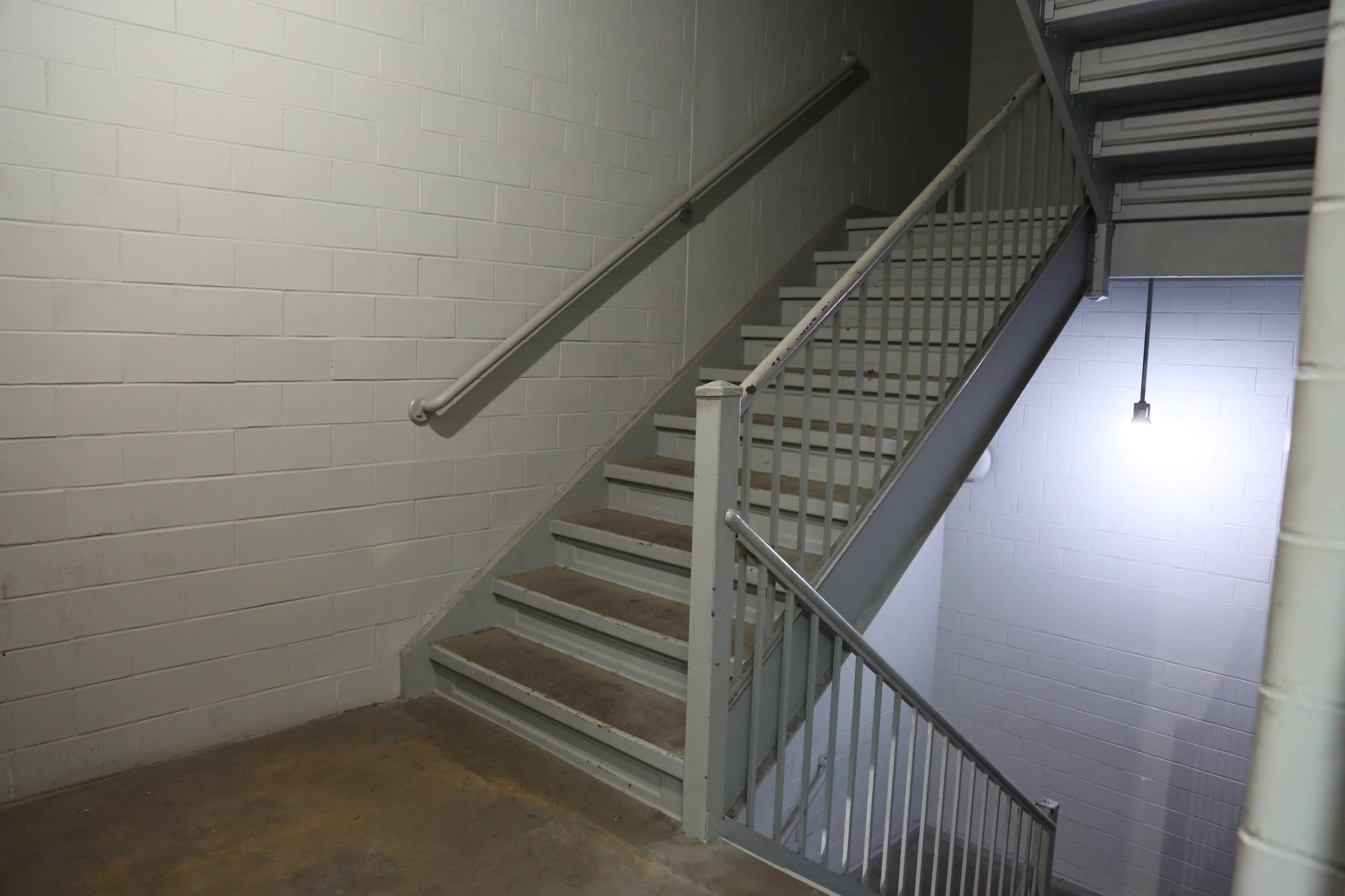 A metal staircase with a handrail ascends alongside a wall in a dimly lit corridor.
