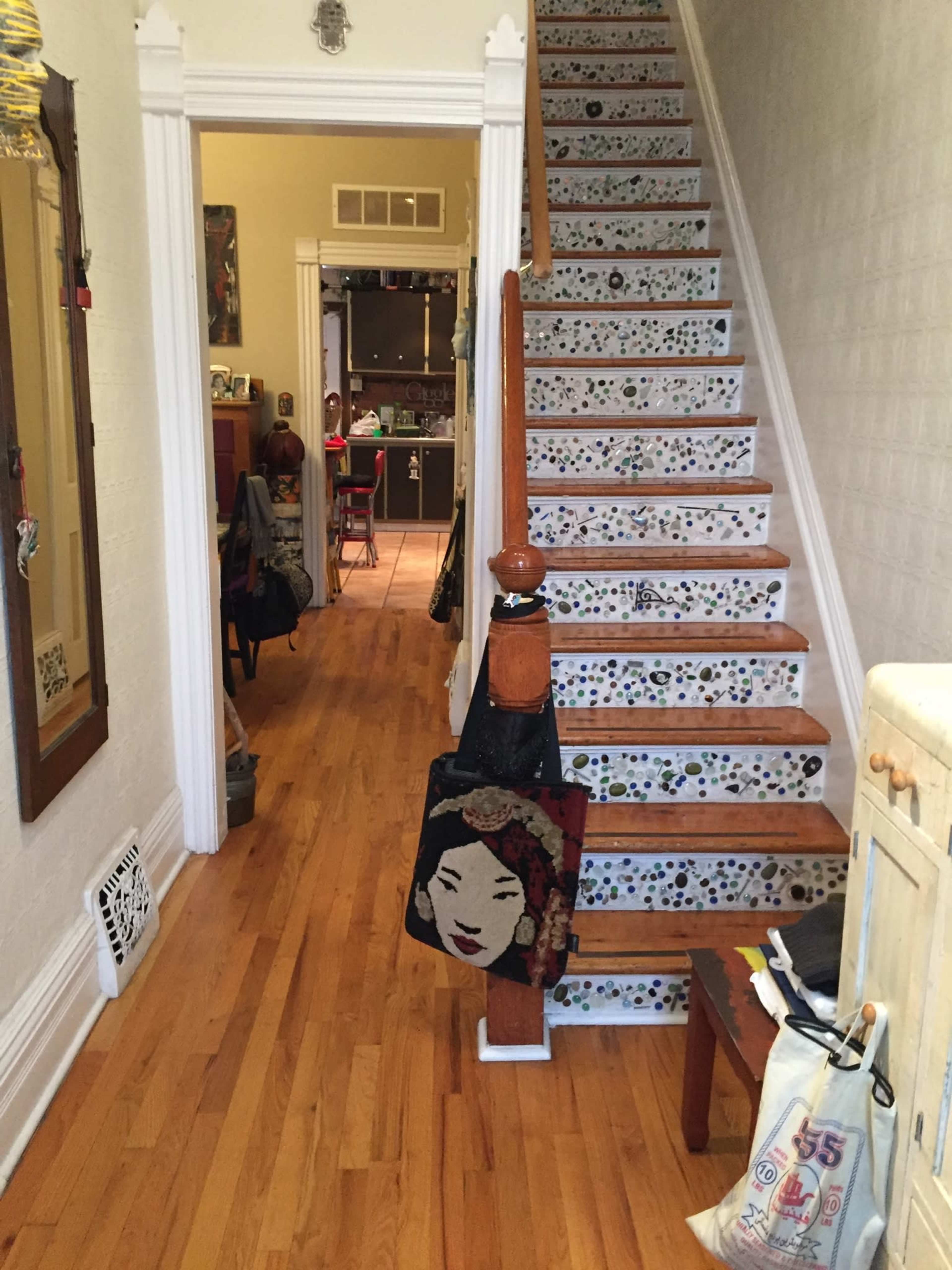 A narrow hallway leading to a staircase adorned with decorative steps, and a glimpse of a kitchen area visible in the background.