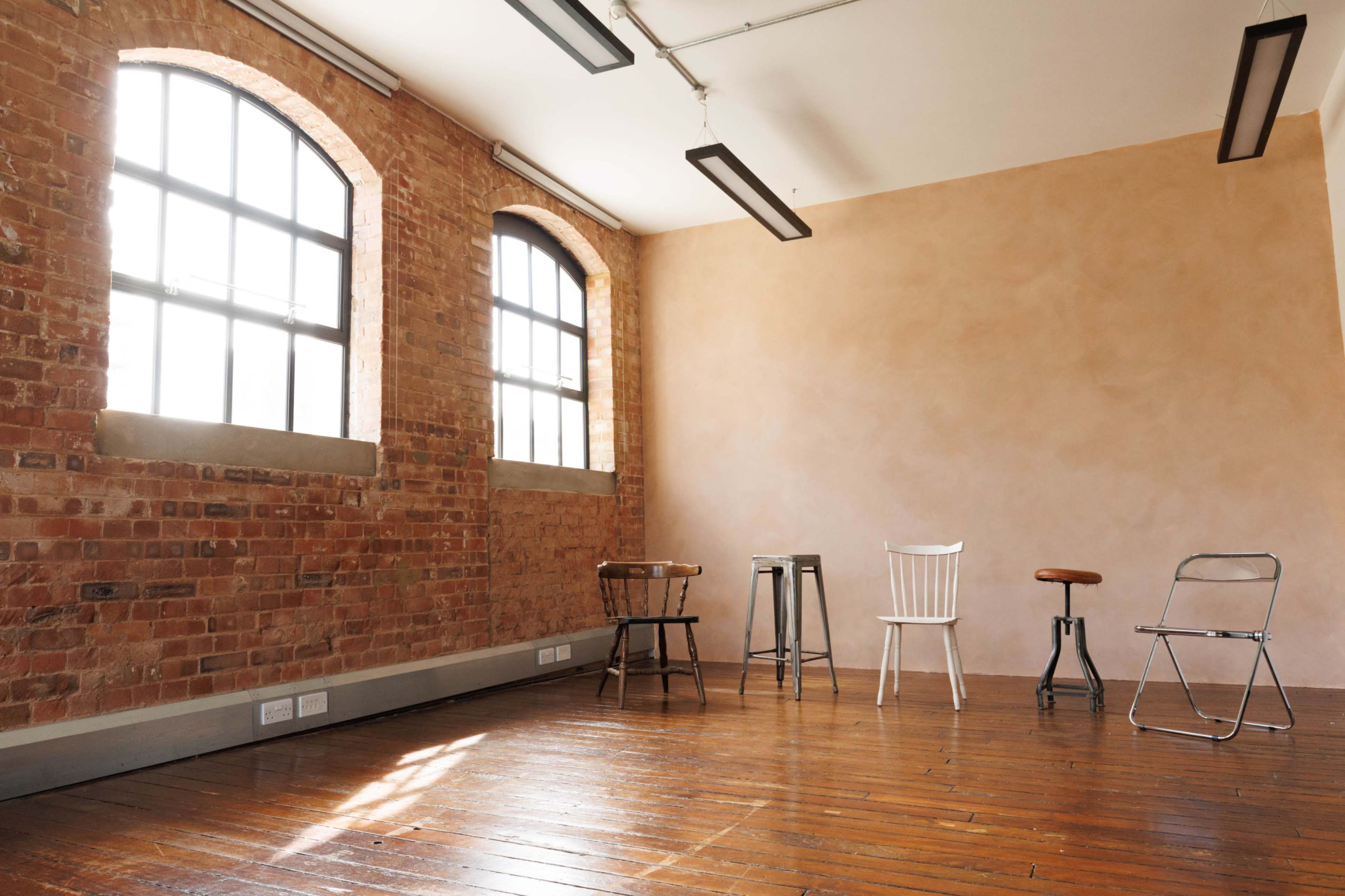A well-lit room features brick walls, wooden flooring, and various metal and wooden chairs arranged around a small table.