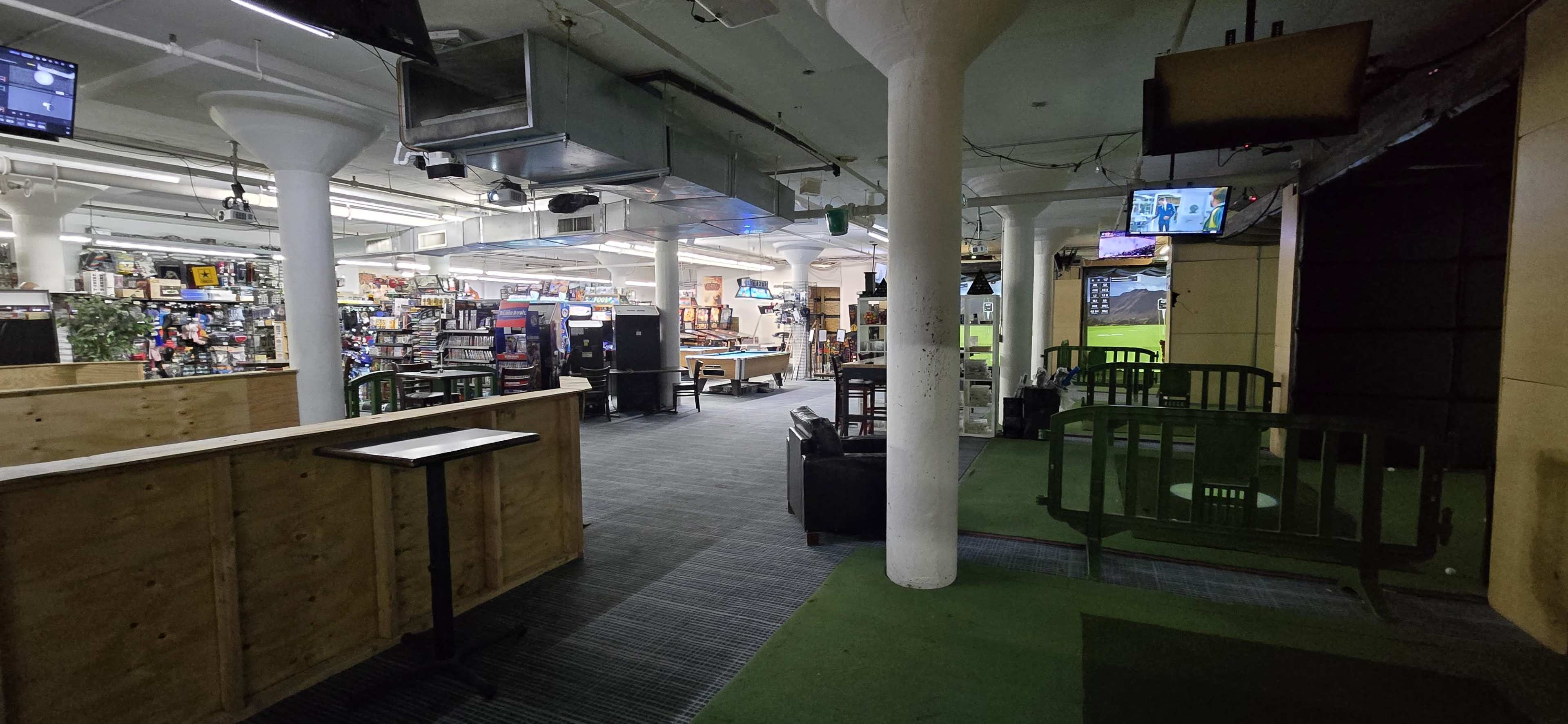 The interior of a retail or entertainment space features various sections with merchandise displays, television screens, and seating areas.