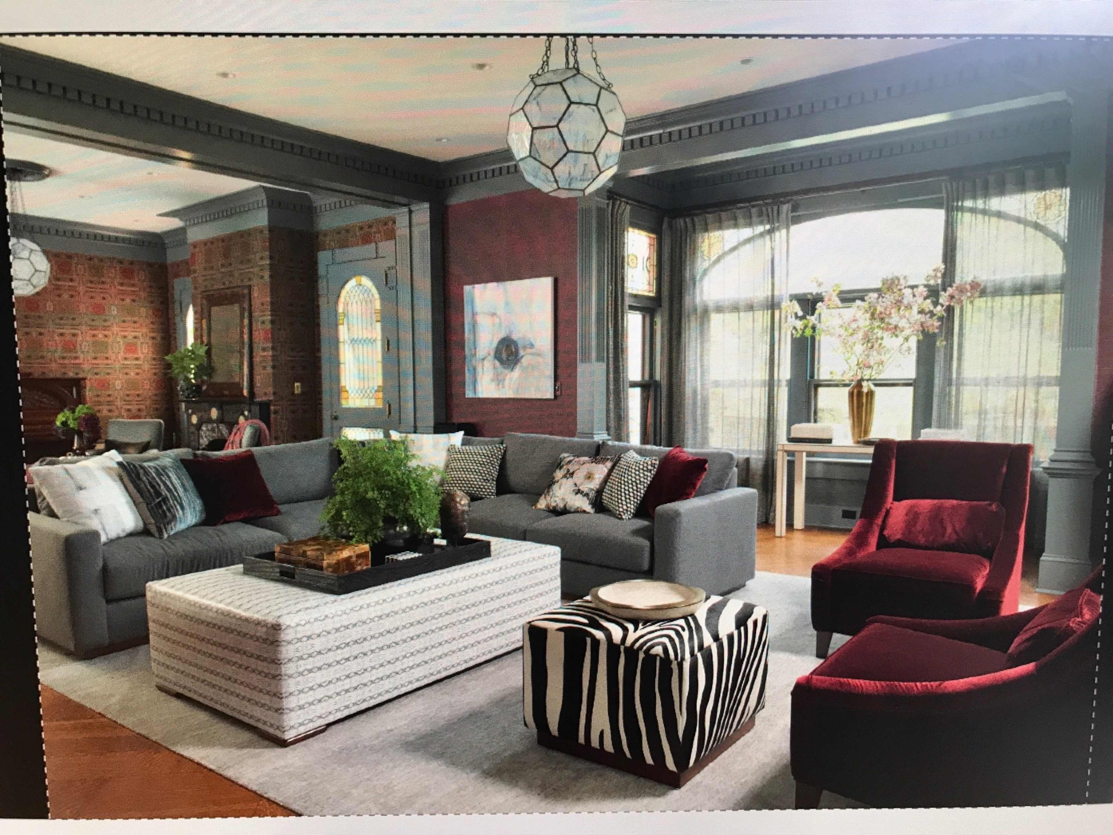 The living room features a gray sectional sofa, a patterned coffee table, and two red accent chairs, with large windows providing natural light.