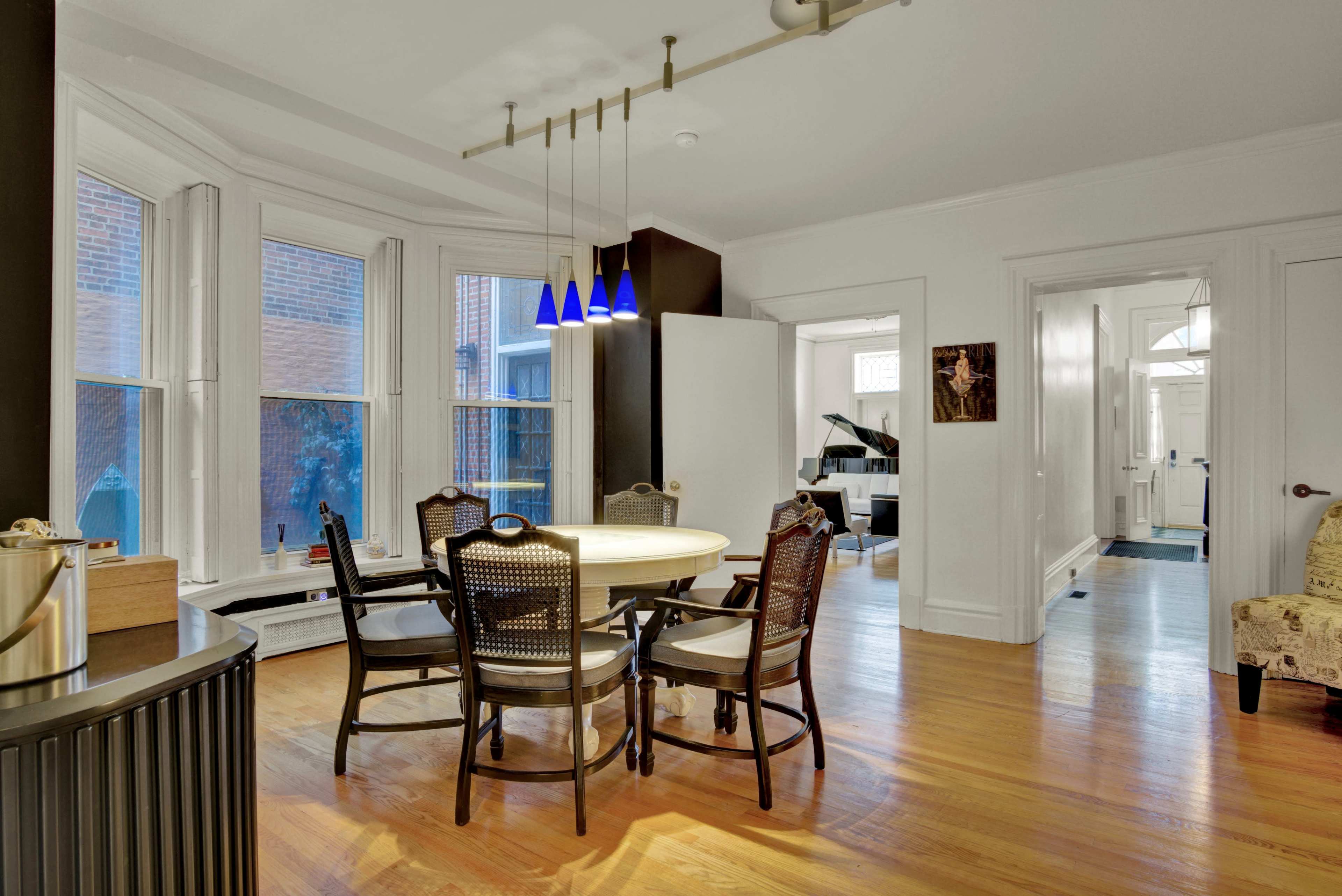 A dining area features a round table surrounded by wooden chairs and is illuminated by three pendant lights.