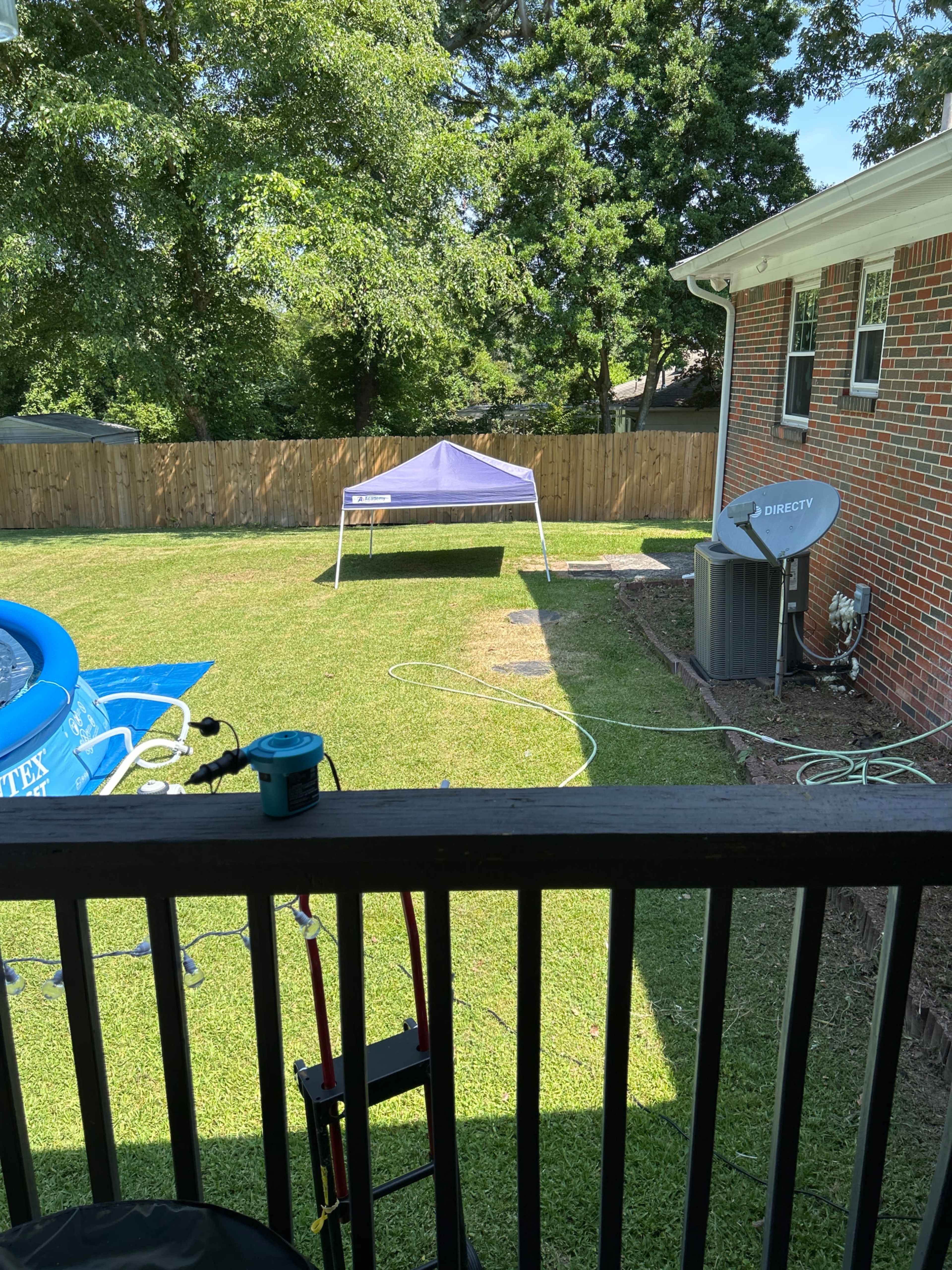A view from a balcony shows a grassy backyard with a tent set up, a blue inflatable pool, and a satellite dish mounted on the side of the house.