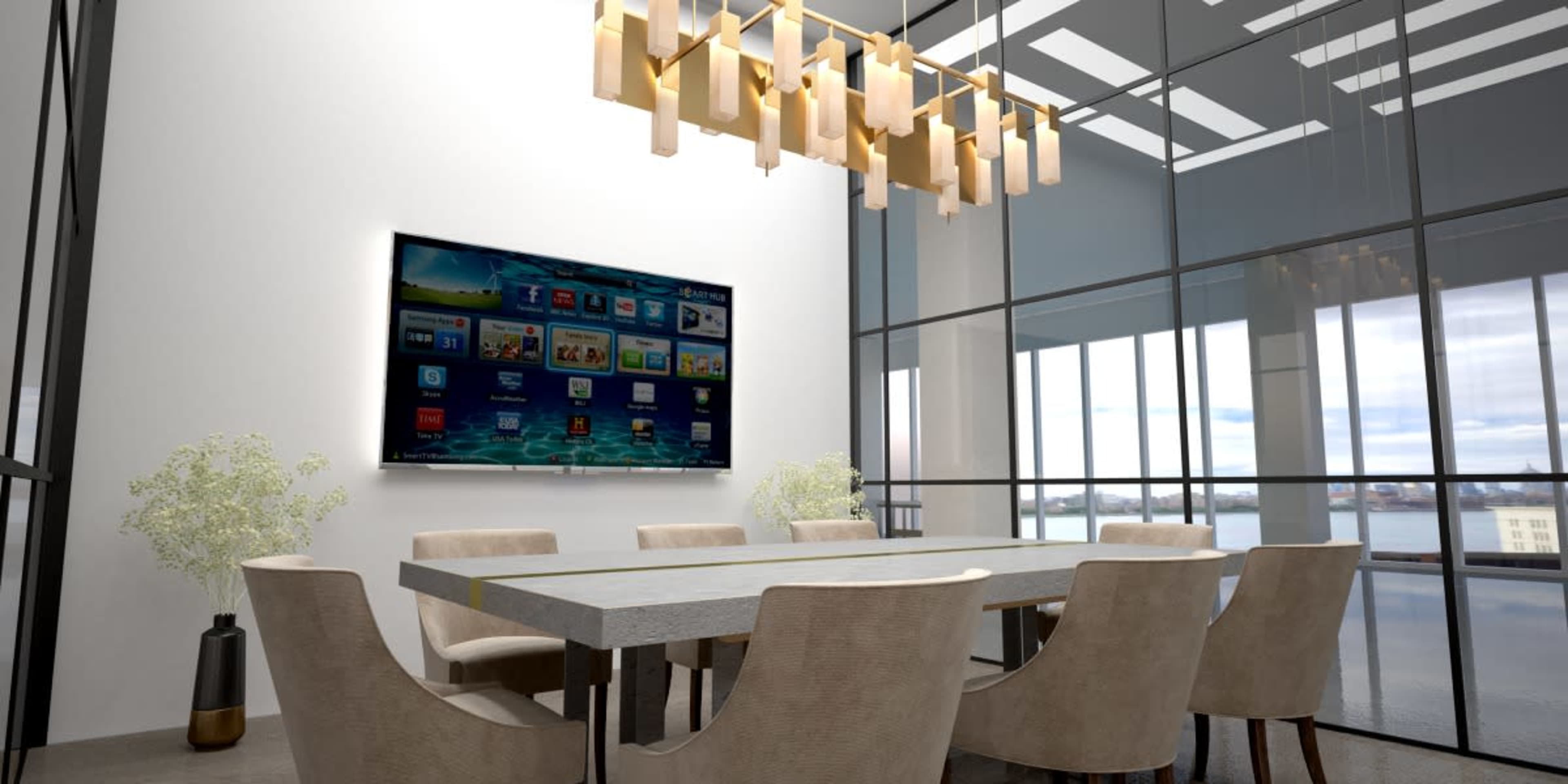 A modern dining area features a rectangular table surrounded by beige chairs, with a large flat-screen TV mounted on the wall and large windows offering a view of the outdoors.