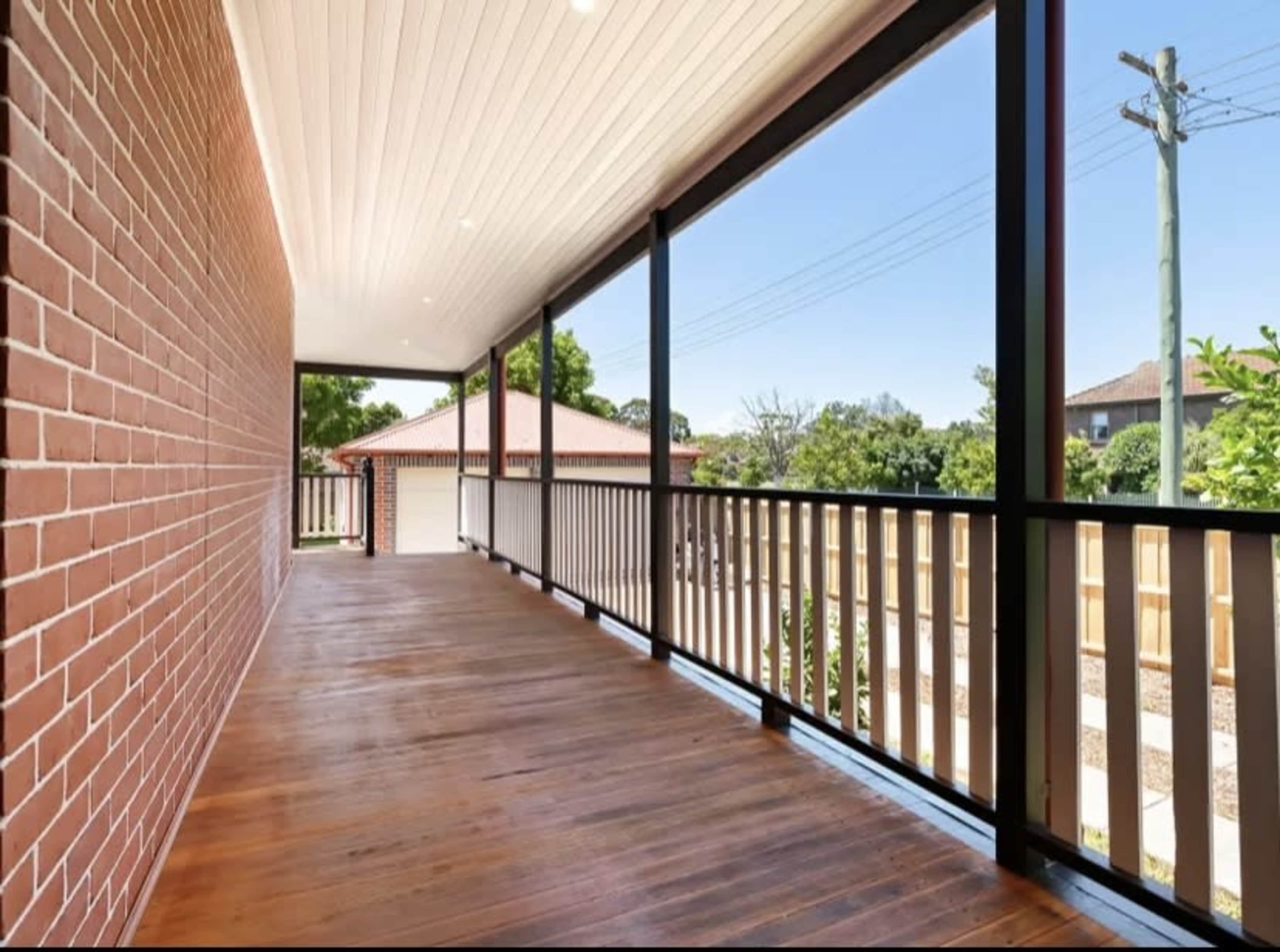 A wooden balcony with brick walls and large windows overlooking a residential area.
