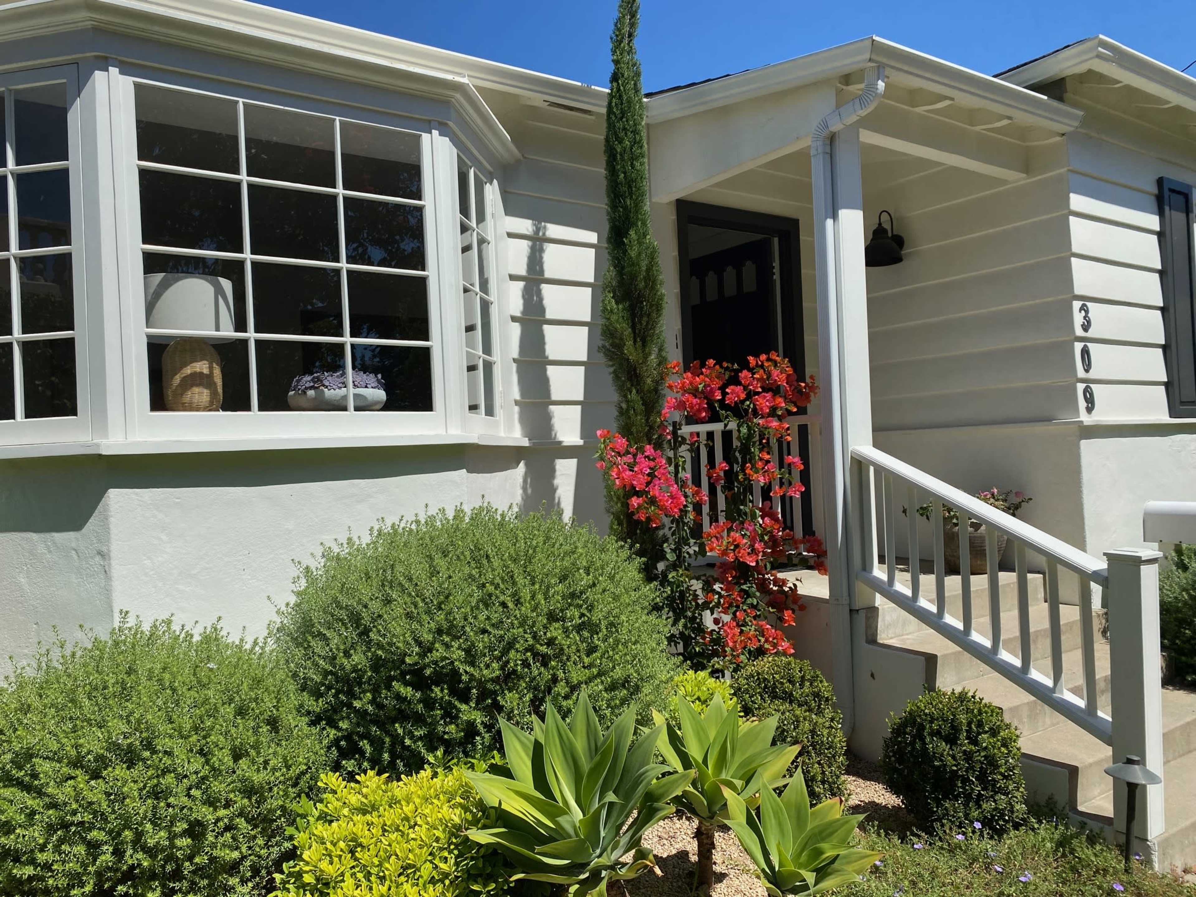 A light-colored house features a decorative front garden with colorful flowers and neatly trimmed shrubs.