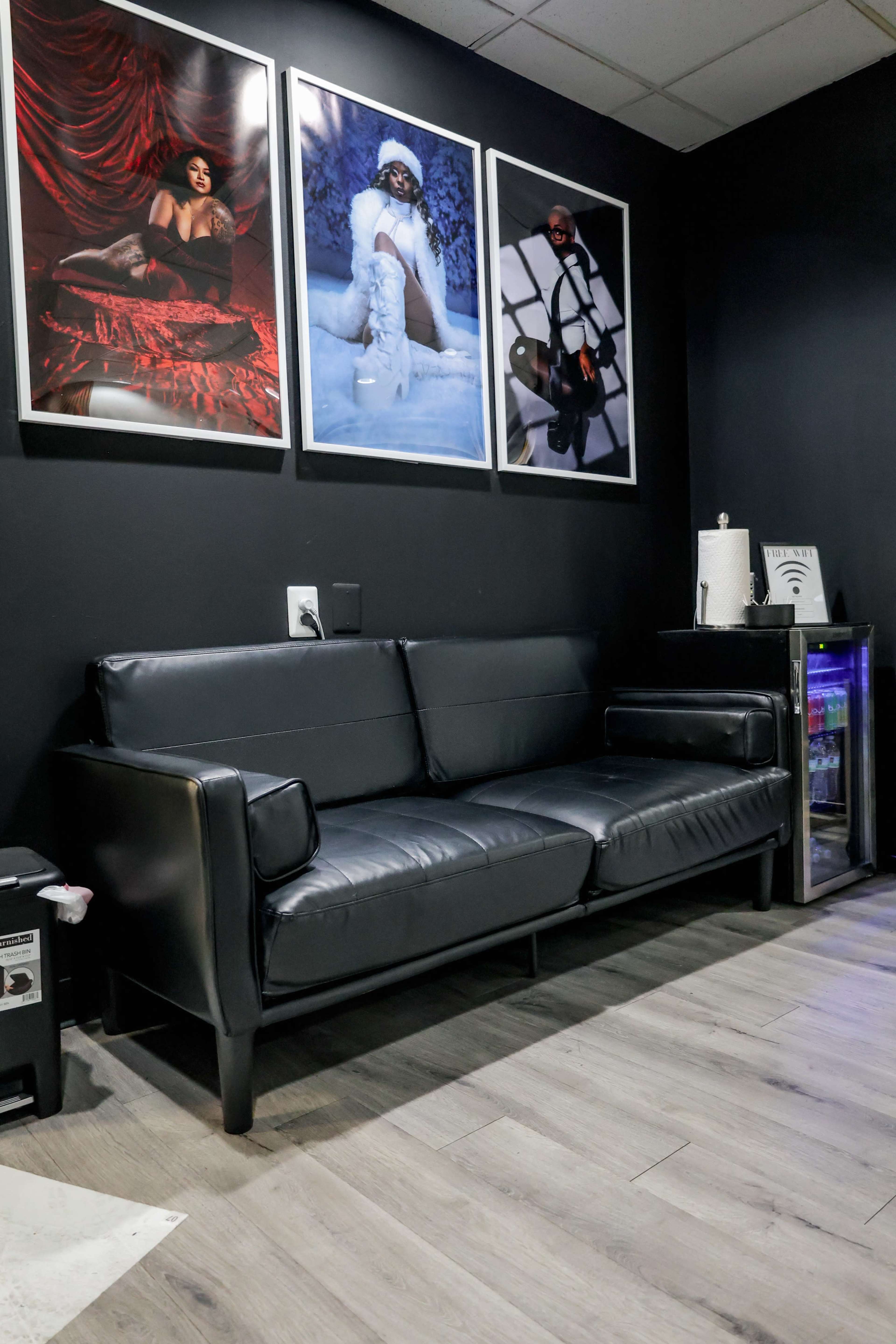 The image shows a black leather couch in a room with dark walls, decorated with three framed photographs on the wall above it.