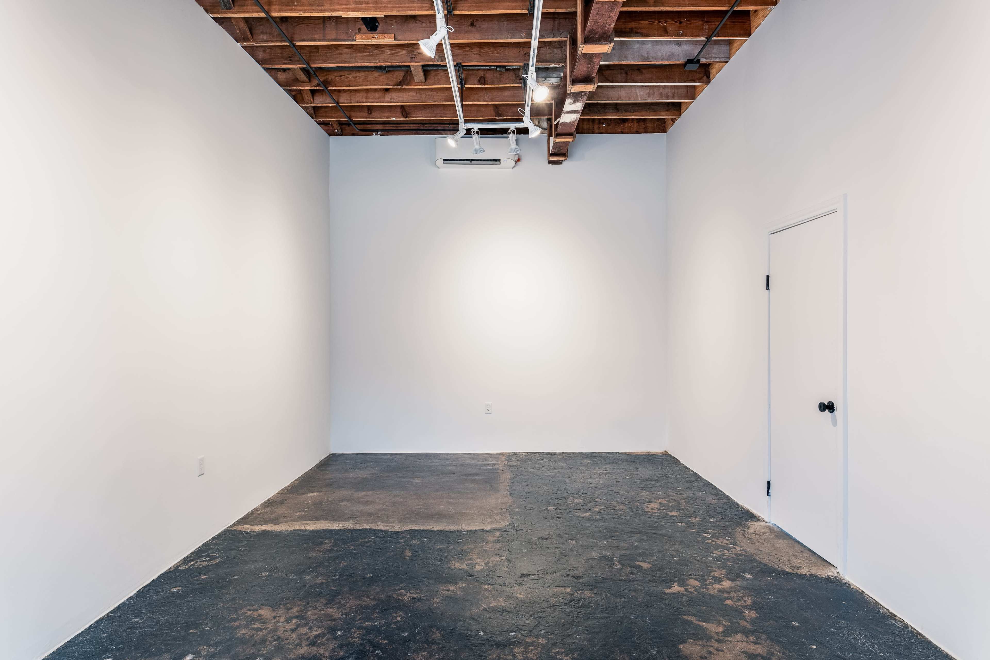An empty room with a concrete floor, white walls, and exposed wooden beams on the ceiling.