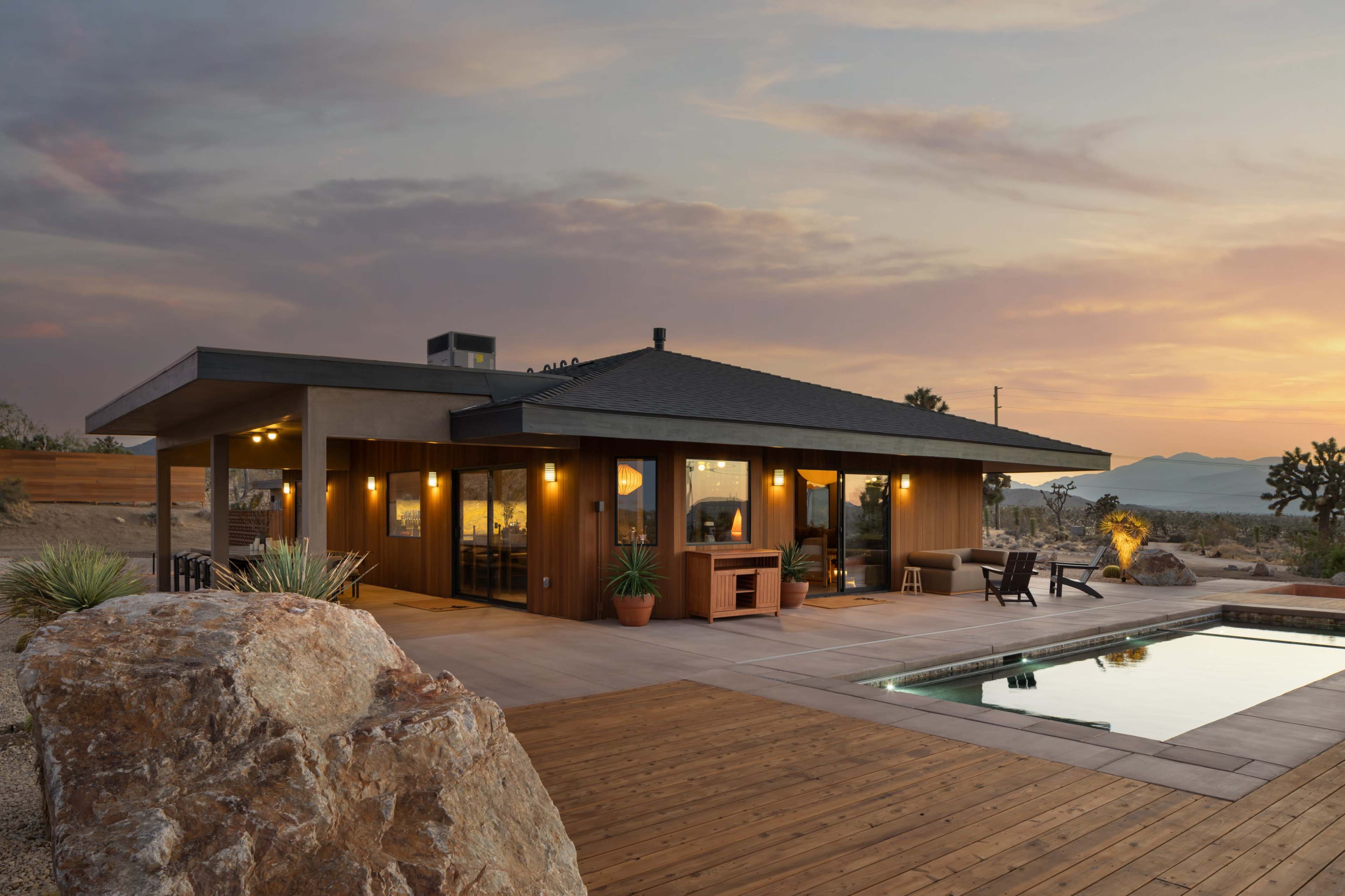 A modern single-story house features large windows, an outdoor patio with a pool, and is surrounded by desert landscaping.