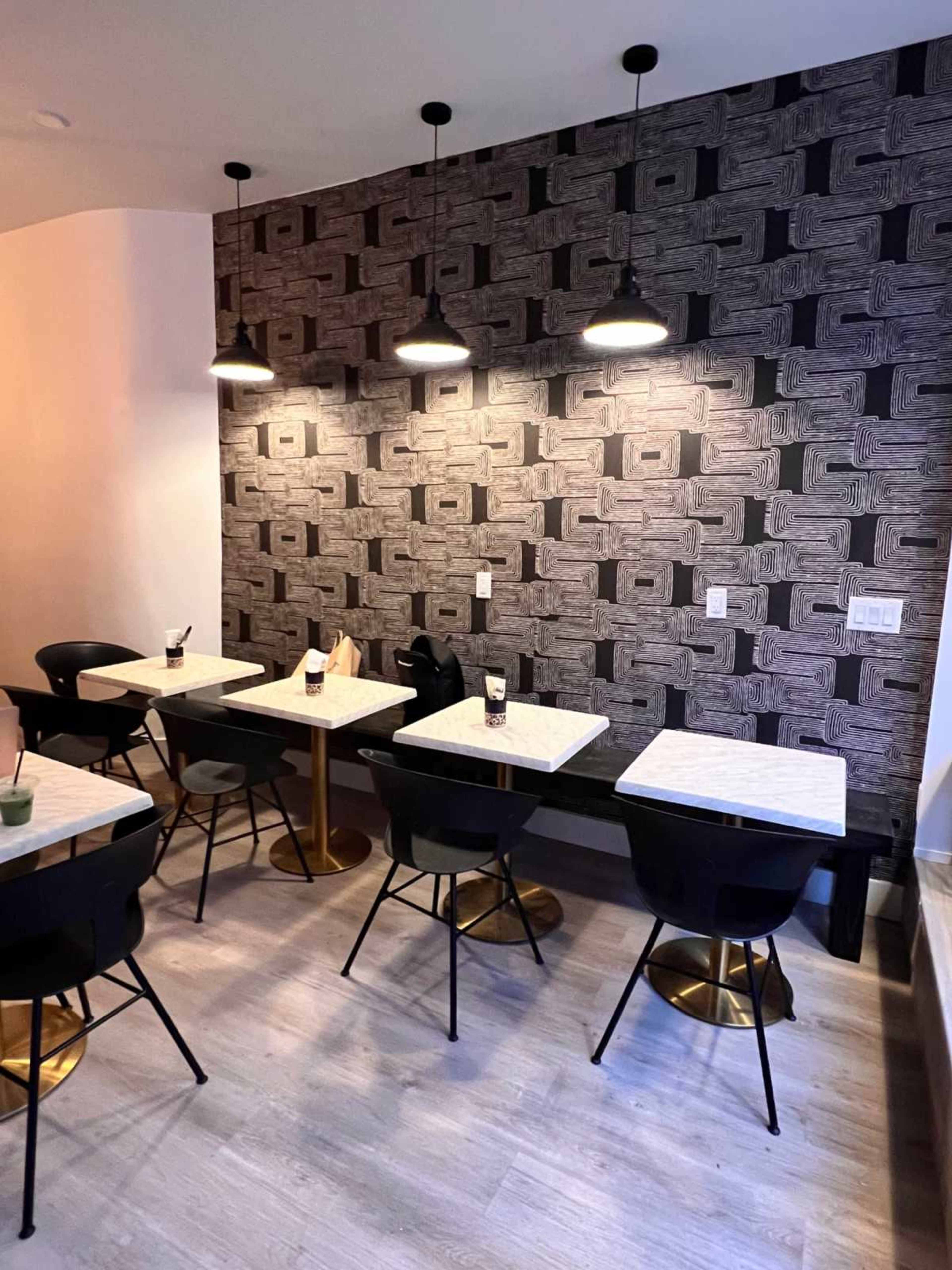 The image shows a modern café interior with several empty tables and chairs, illuminated by pendant lights against a patterned wallpaper.