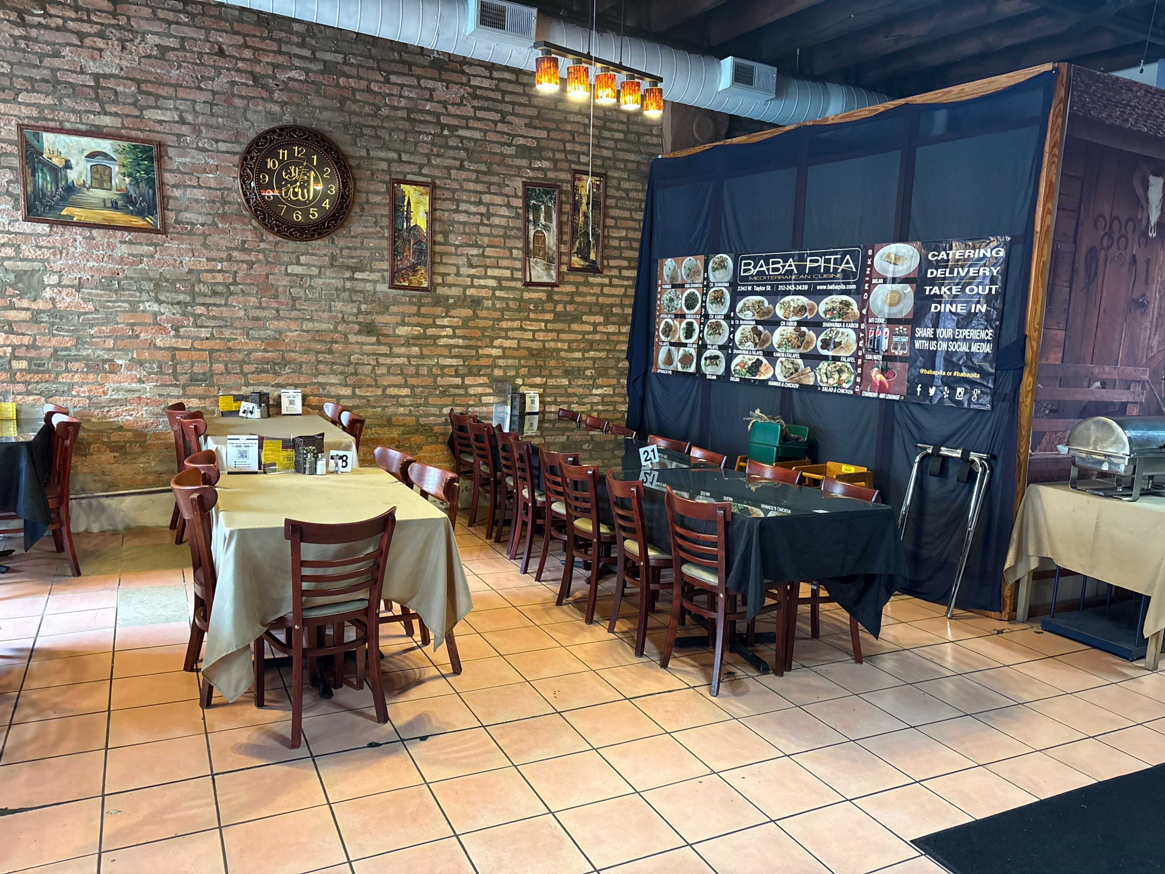 The image shows the interior of a restaurant featuring wooden tables and chairs, with a partially visible menu board and decorative brick walls.