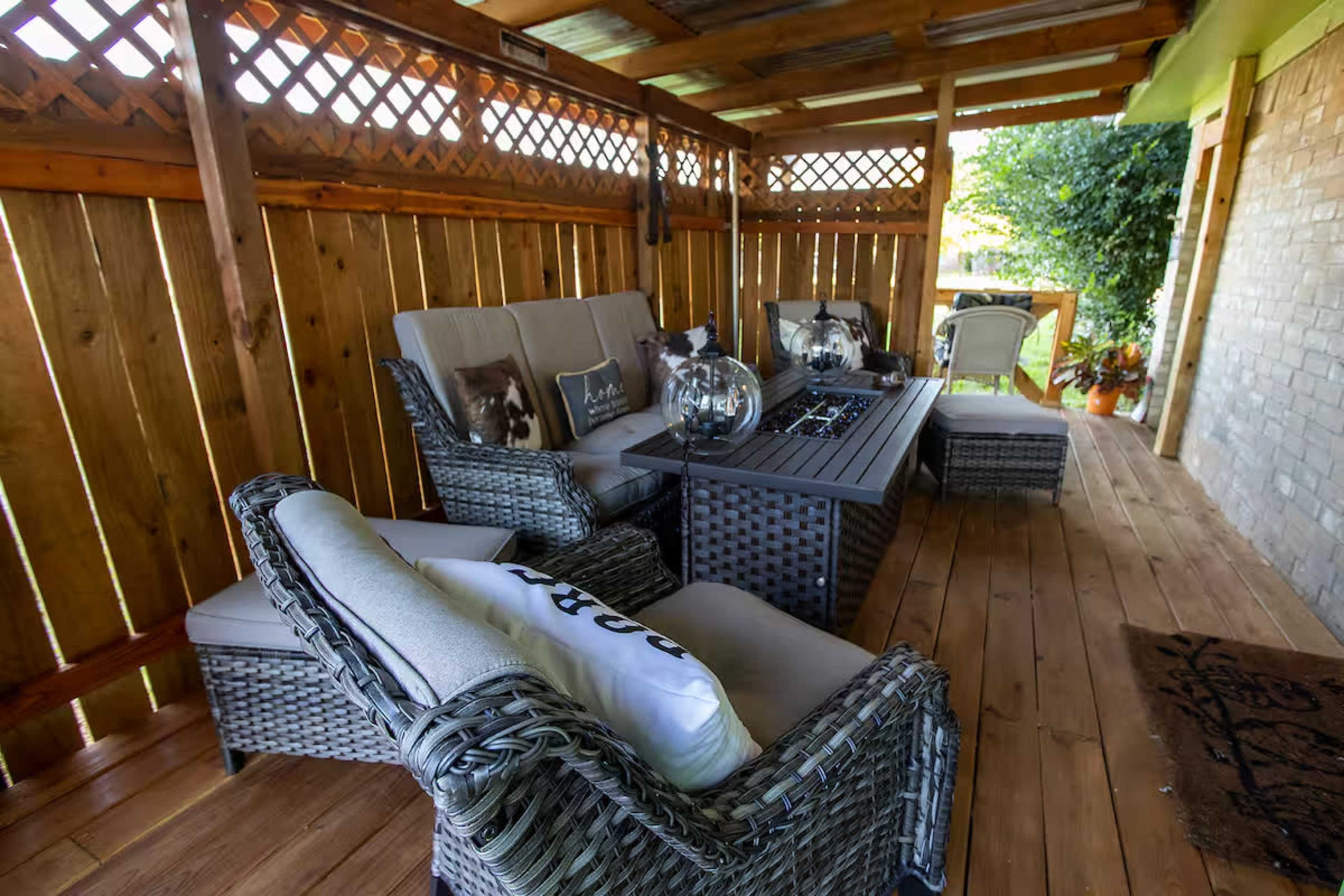 The image shows a covered outdoor patio with woven furniture arranged around a central fire table.