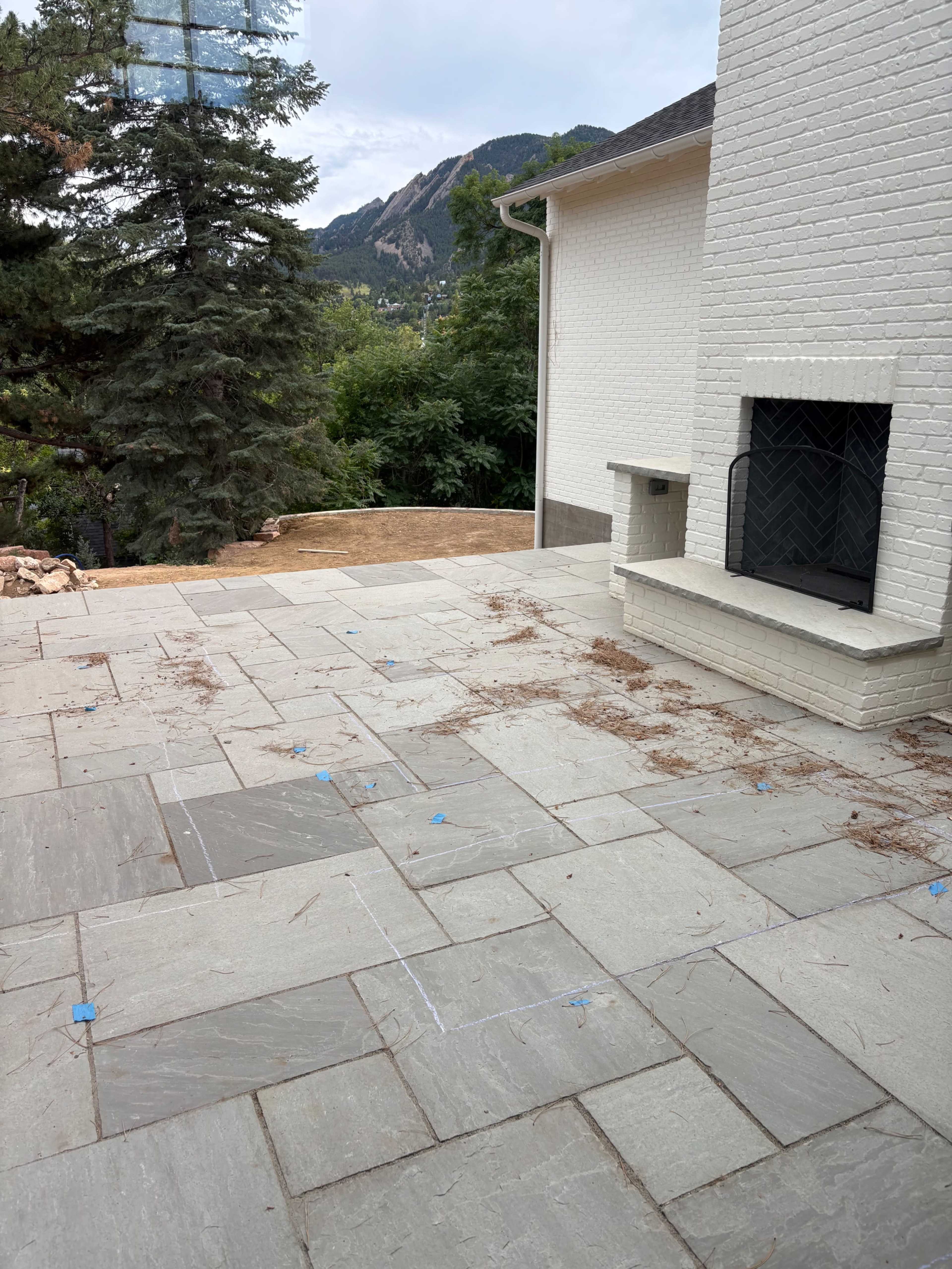 The image shows a patio area with stone pavers, a white brick house on one side, and a mountainous landscape in the background.