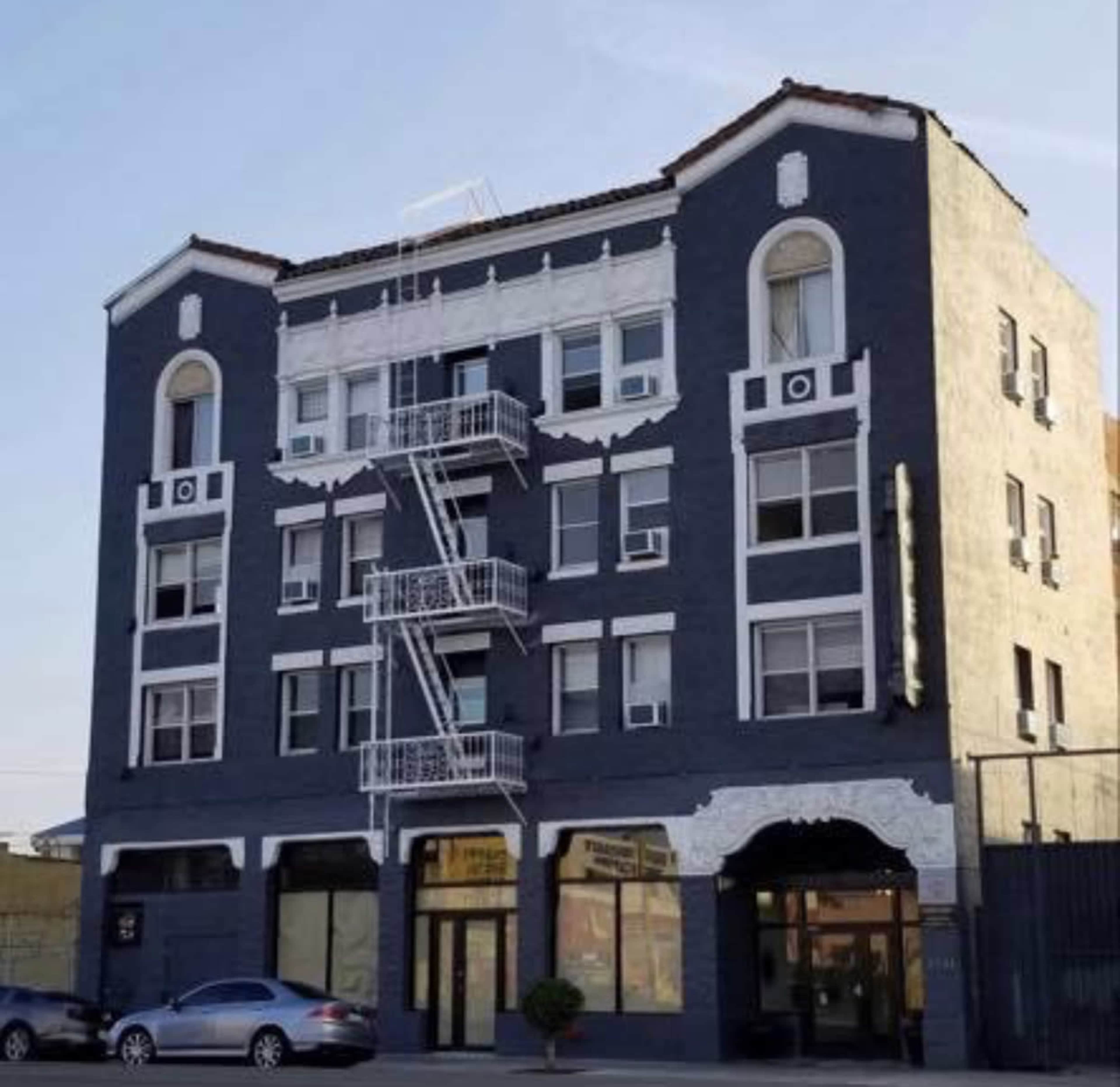 A four-story, blue building featuring white architectural accents and a metal fire escape, with storefronts at the ground level.