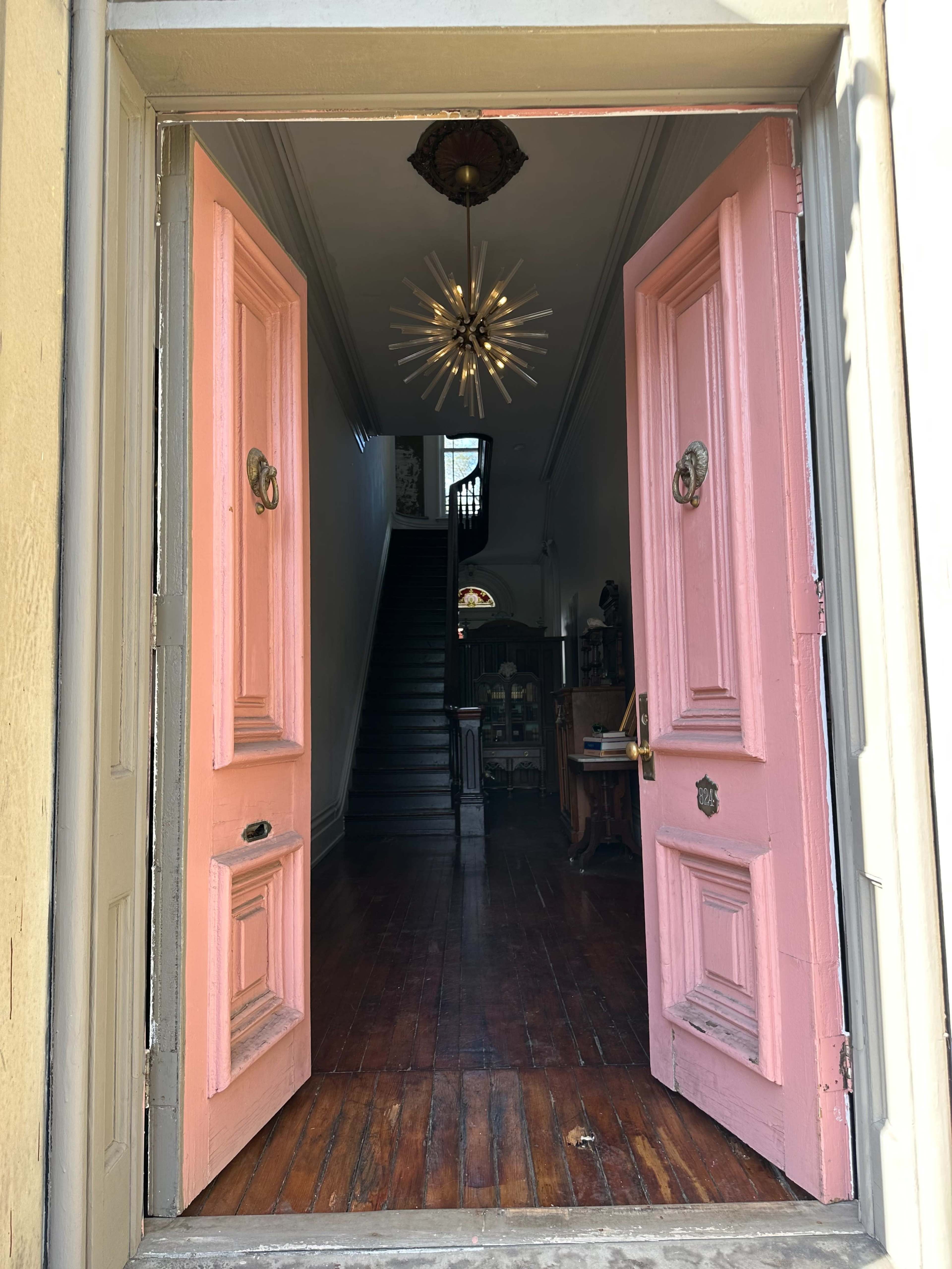 The image shows a vibrant pink double door opening into a hallway with wooden flooring and stairs leading upward.