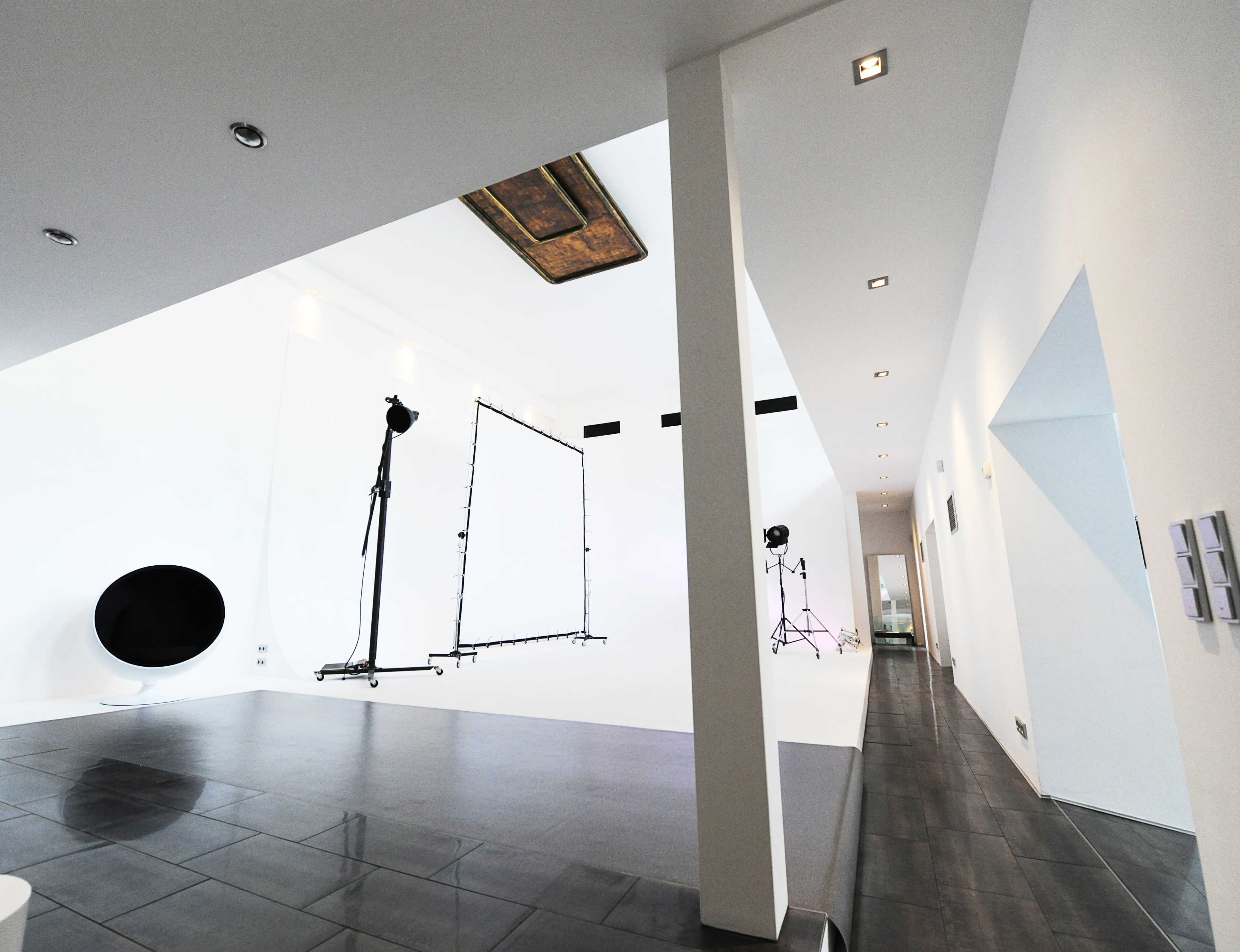 The image shows a spacious studio with white walls, a large backdrop setup, and soft lighting, featuring a polished floor and minimalist design elements.