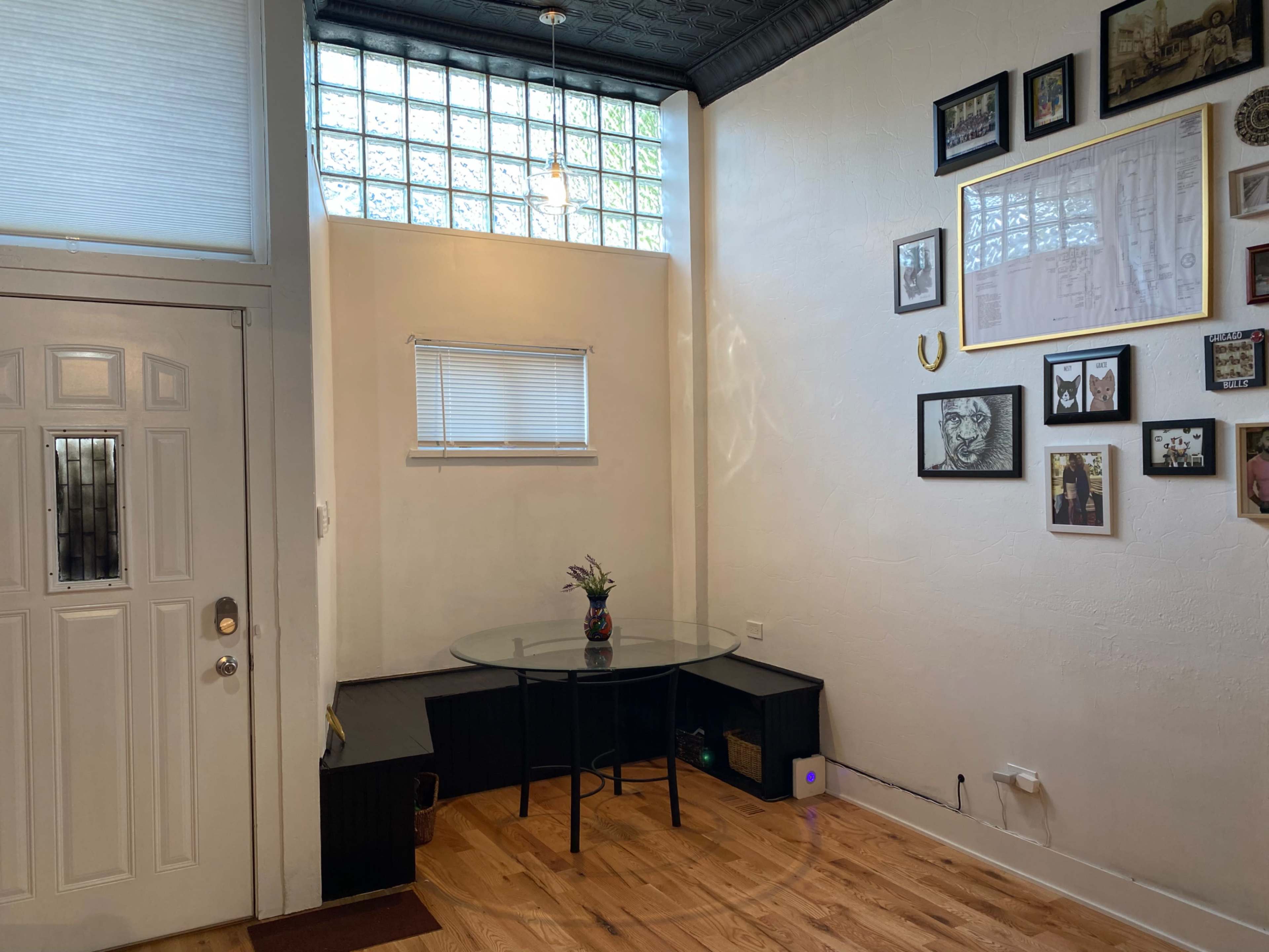 An entryway with a round glass table, a small storage unit, and a wall adorned with various framed photos.
