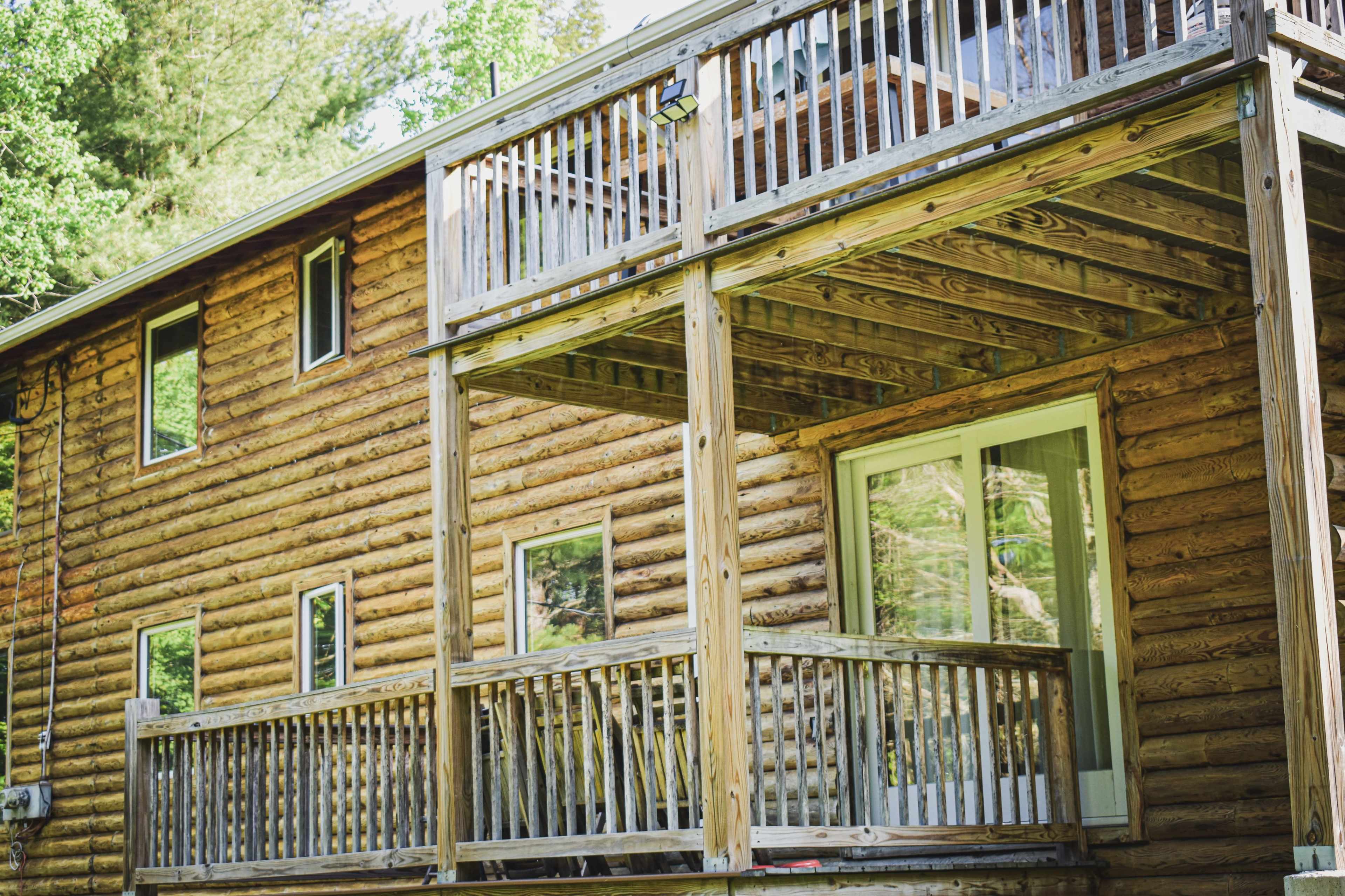 The image shows a wooden cabin with two levels, featuring exterior balconies and large windows.