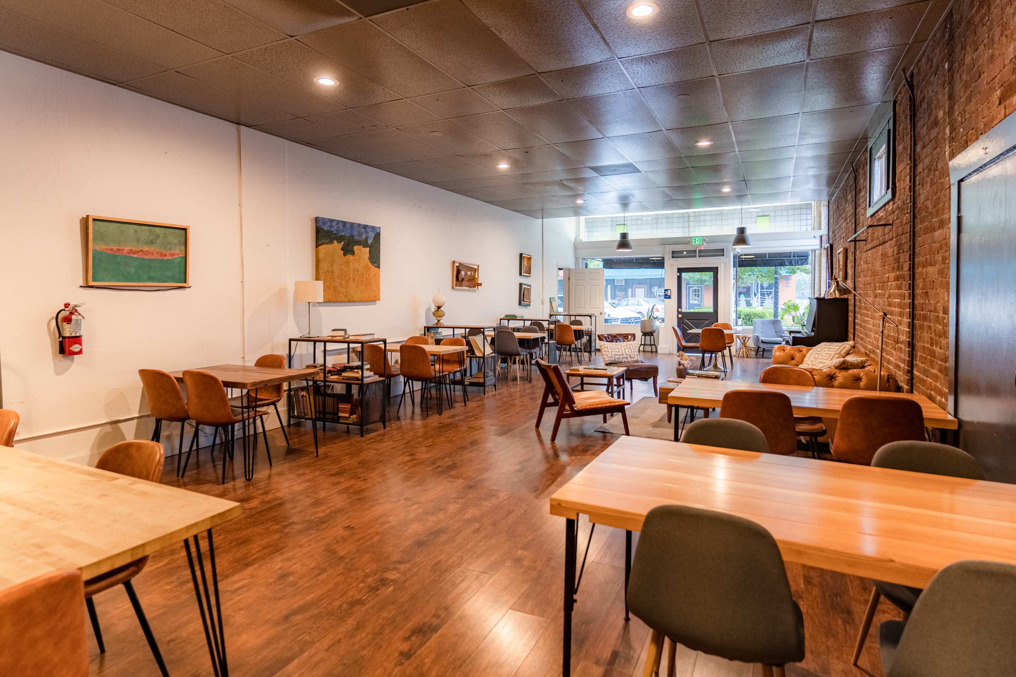 The image shows an interior of a cafe or restaurant featuring wooden tables and chairs, against a backdrop of brick and white walls.