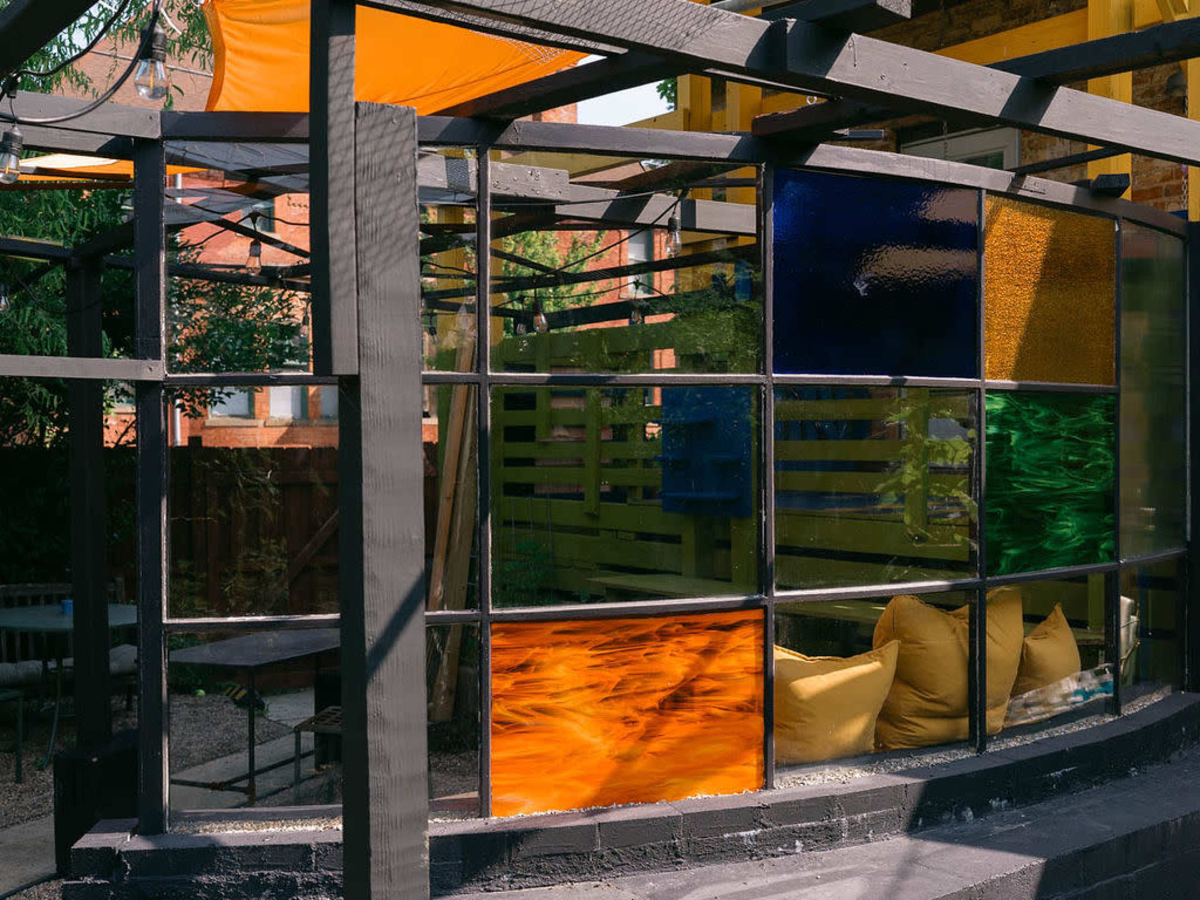 The image shows a segmented glass wall featuring panels of various colors, surrounded by a landscaping of greenery and outdoor seating.