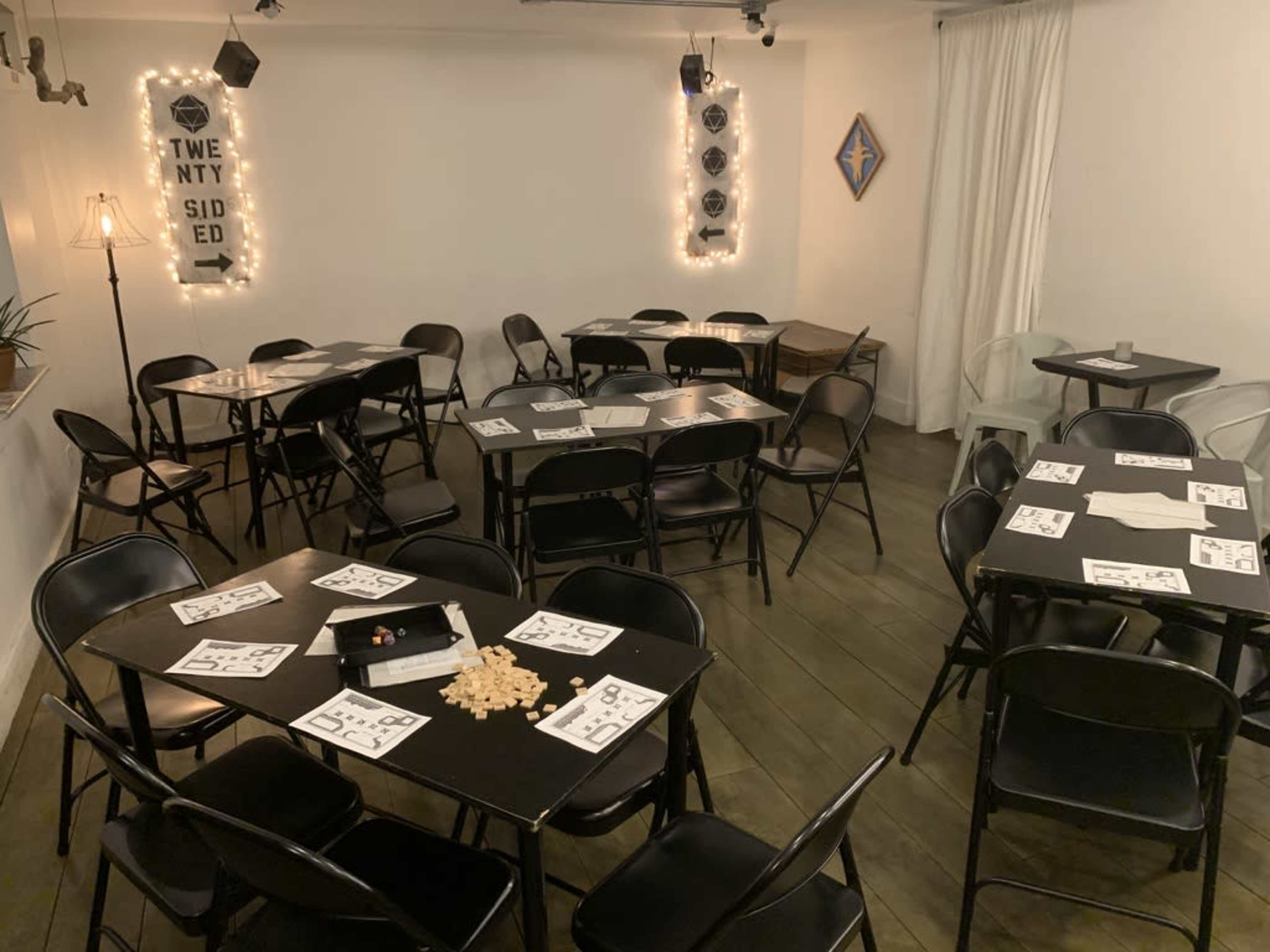 A room with multiple black folding tables and chairs arranged for an event, featuring decorations on the walls and a soft lighting setup.