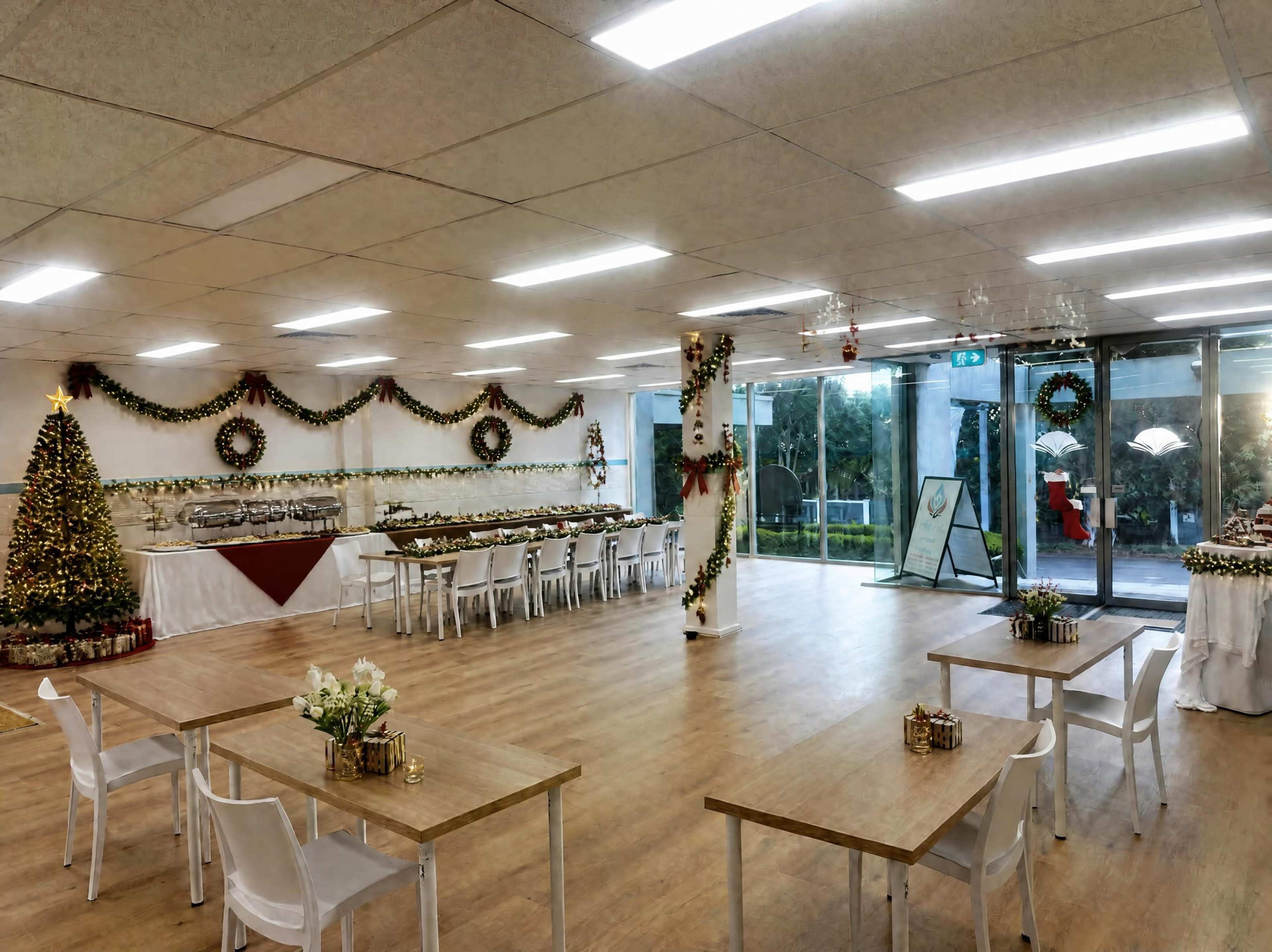 The image shows a spacious event room decorated for a festive celebration, featuring a Christmas tree, garlands, and tables set for dining.