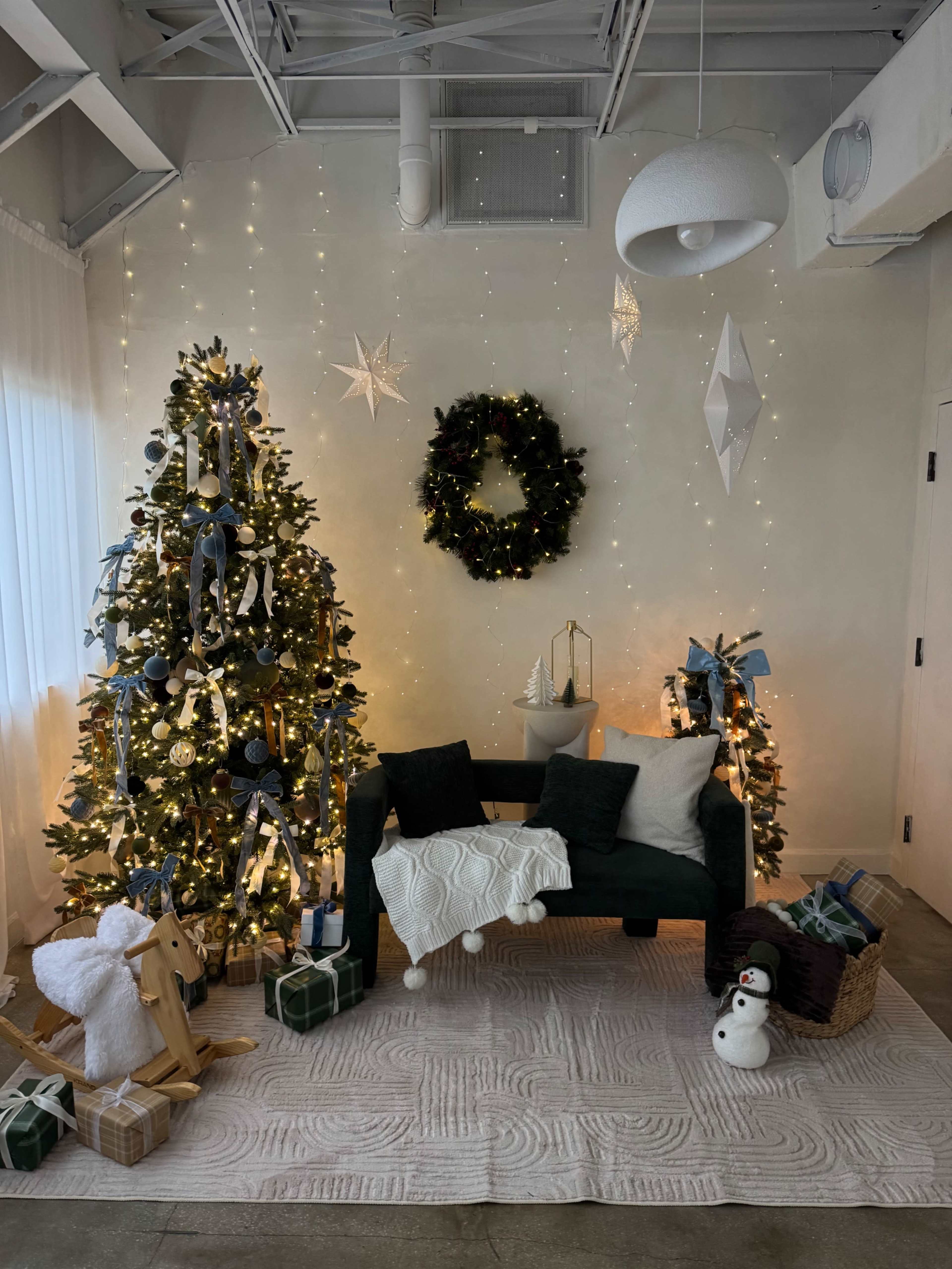 The image depicts a festive corner with a decorated Christmas tree, a small sofa adorned with a blanket, and gifts, all surrounded by twinkling lights and holiday decorations.
