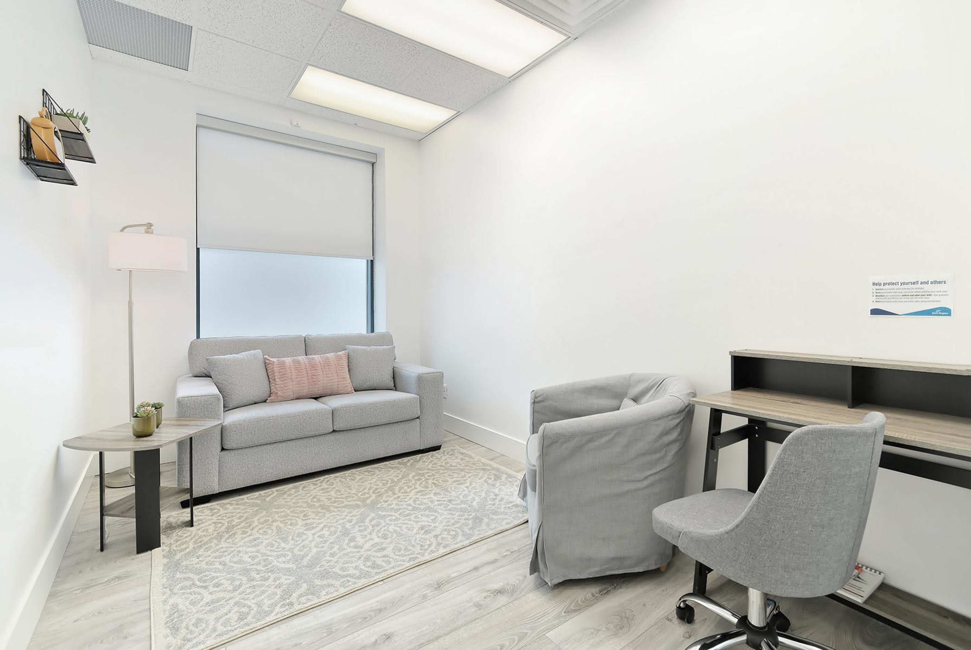 A small, neatly arranged office space with a couch, a side table, a desk, and a chair.