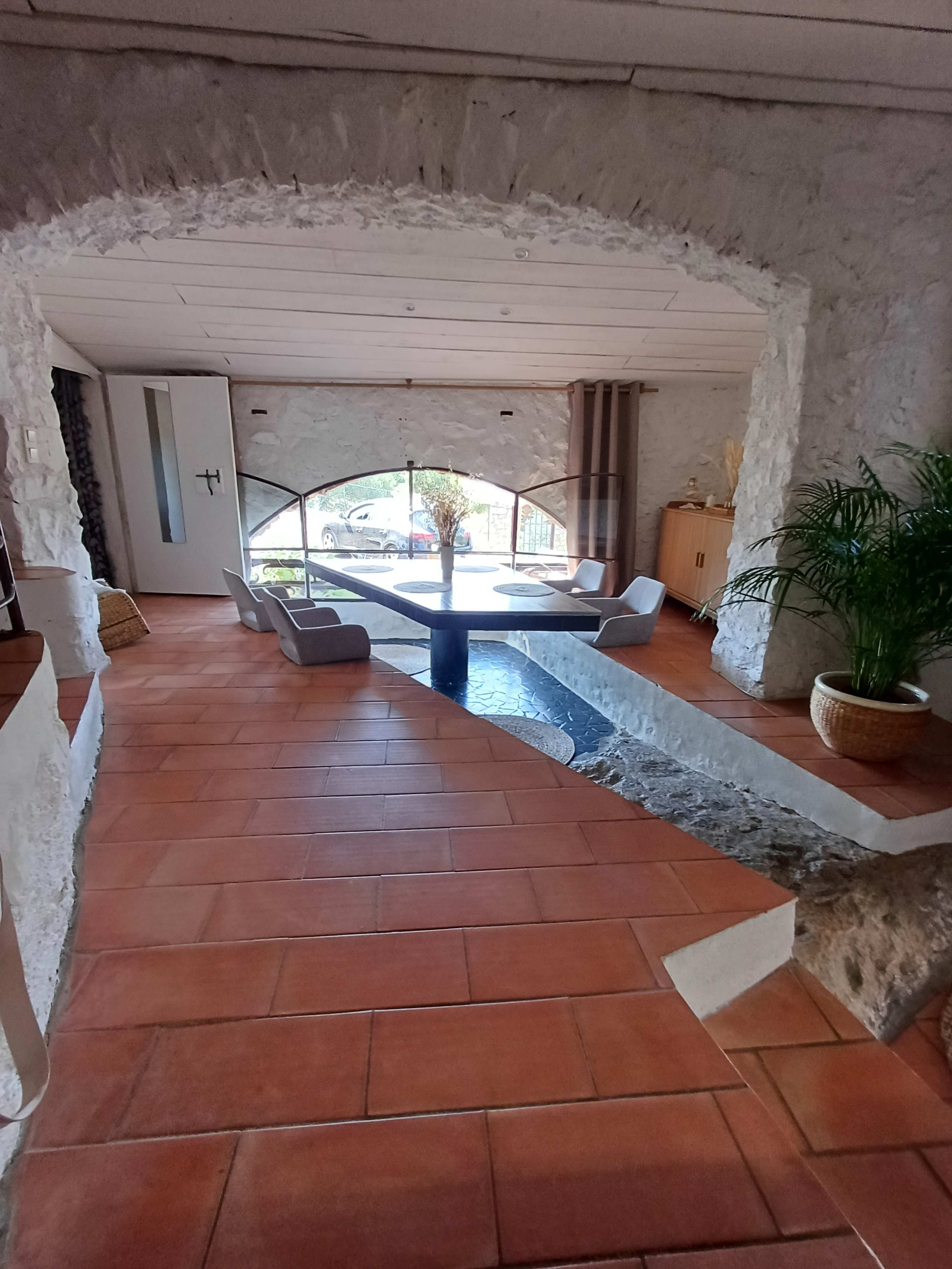 The image shows a spacious interior room with stone arches, a large window letting in natural light, and a unique water feature integrated into the floor.