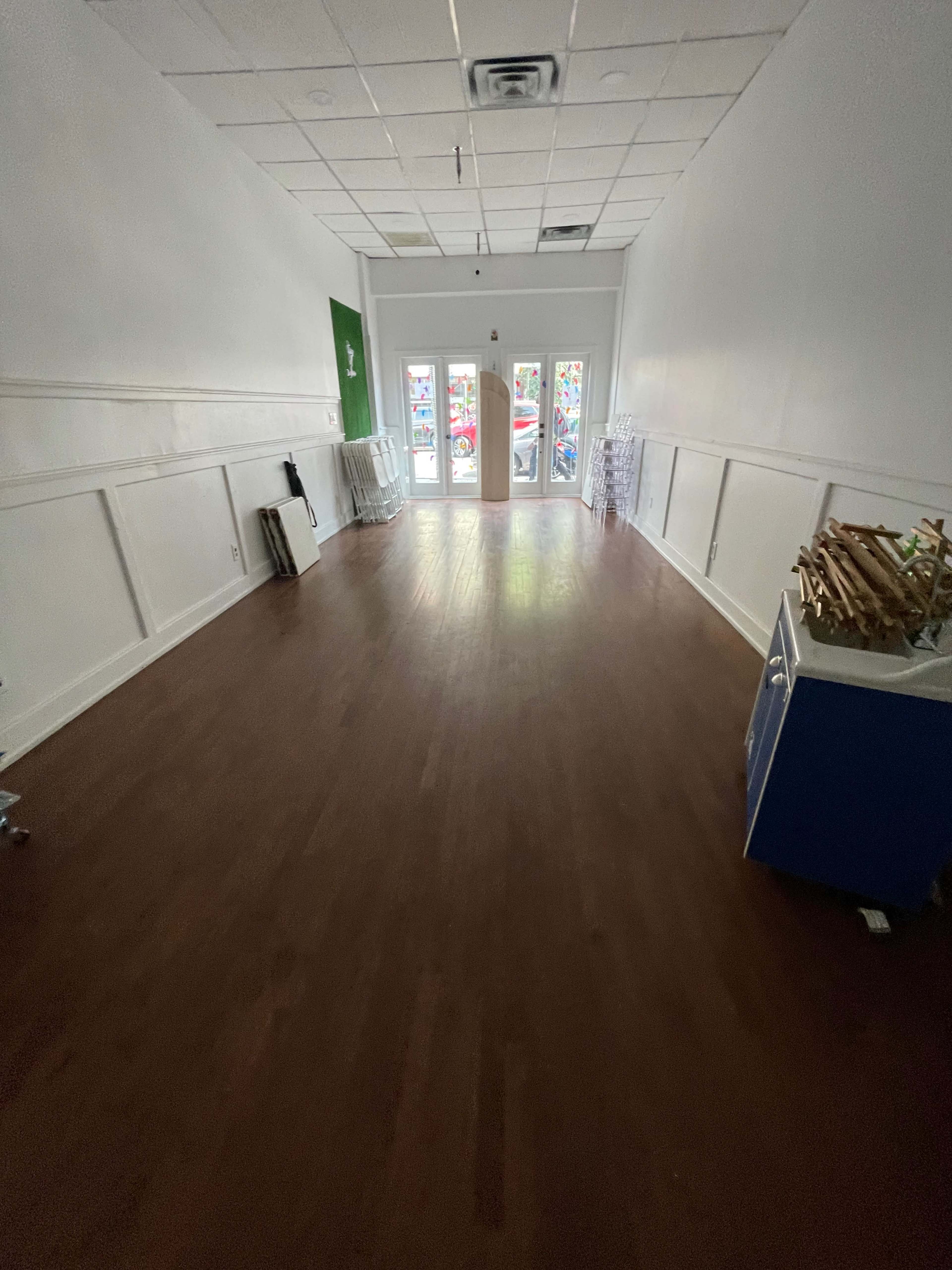 A spacious, empty retail space with wooden flooring and large windows at the front.