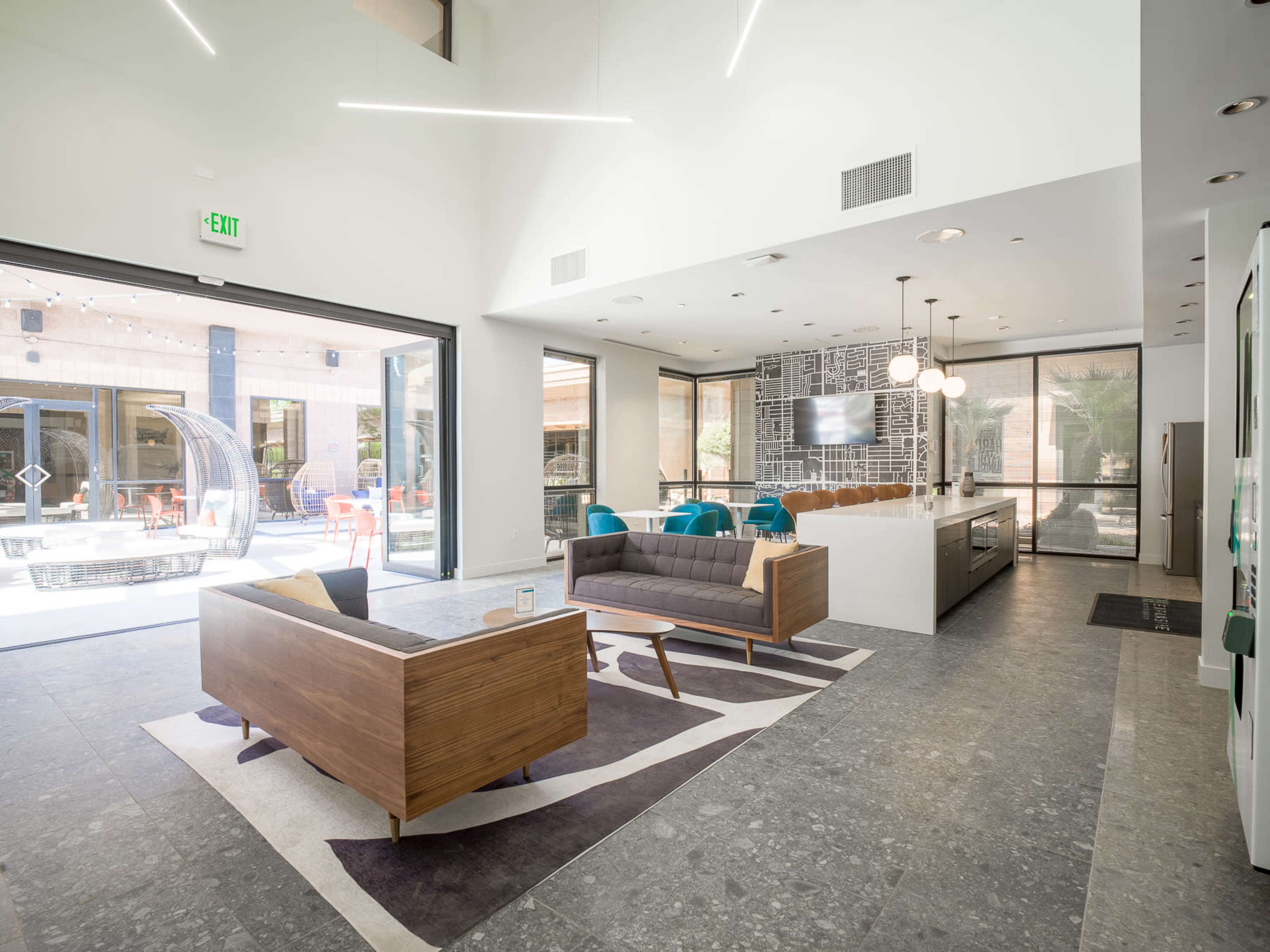 The image shows a modern lounge area that features a seating arrangement with a wooden coffee table, a gray sofa, and a view of an outdoor space through large glass doors.