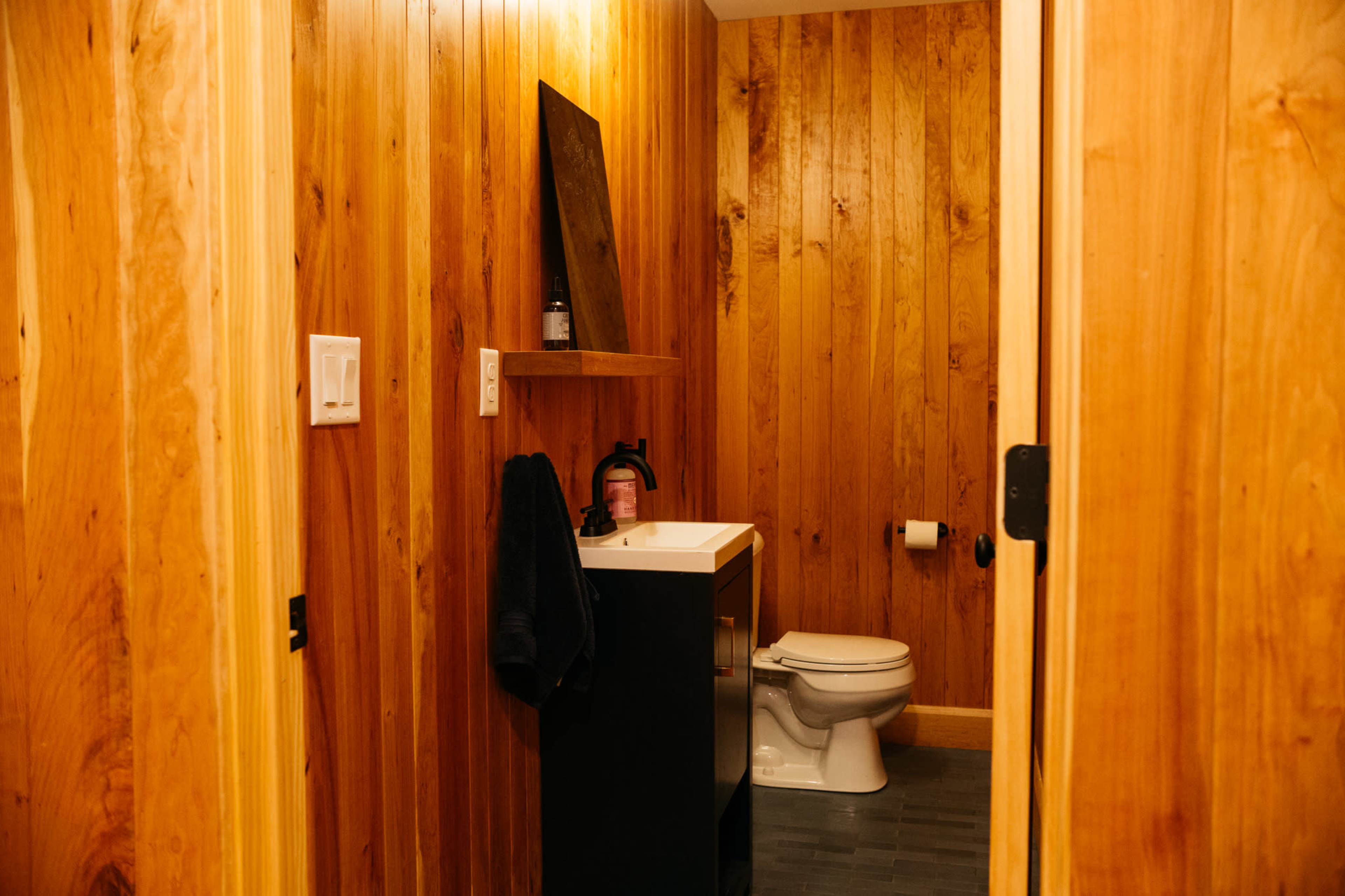 A small bathroom with wooden walls, a black vanity with a sink, a toilet, and a towel hanging on the wall.