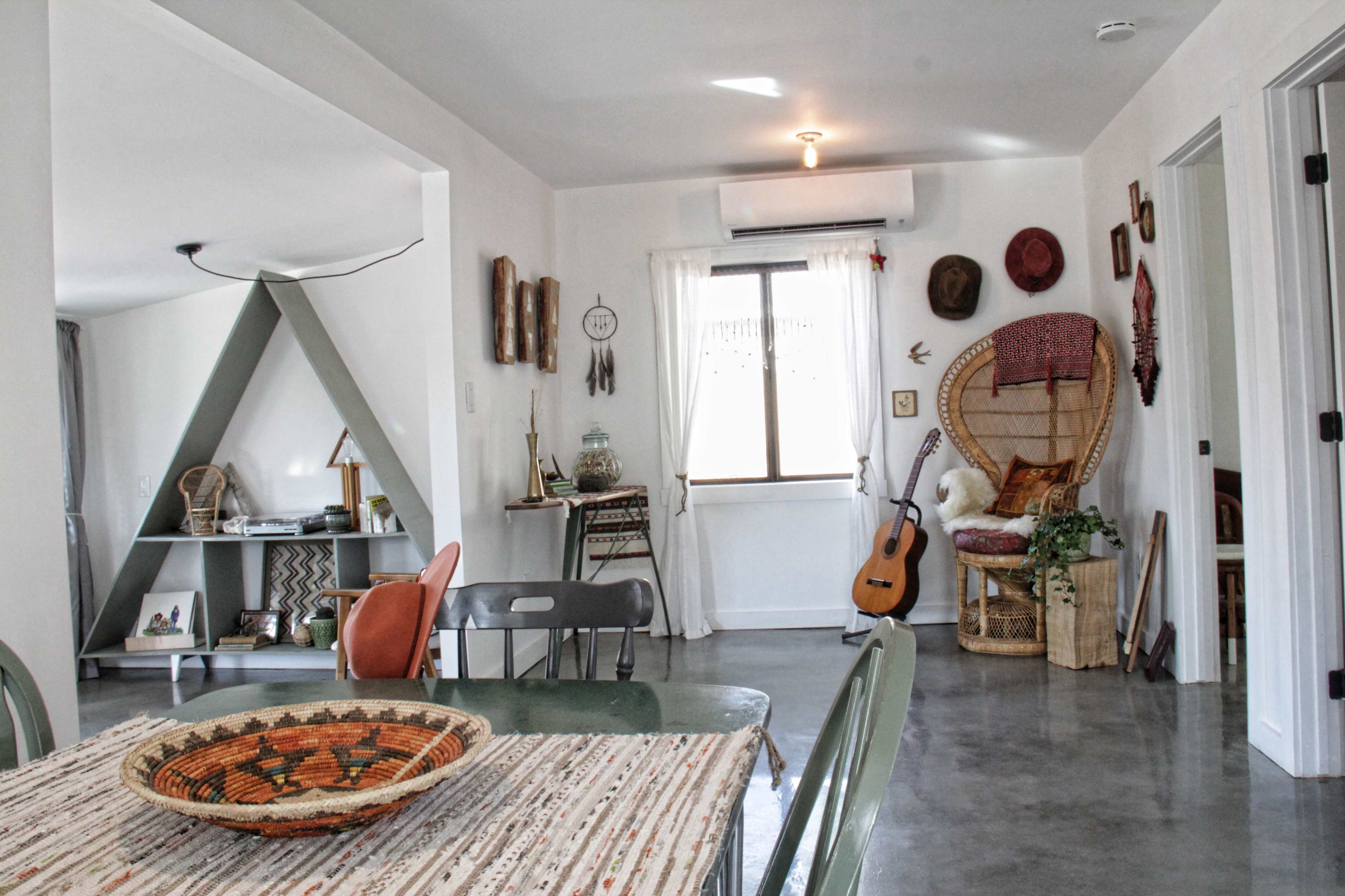 An interior living space featuring a dining table, a decorative bookshelf, a cozy seating area with a guitar, and various wall ornaments.