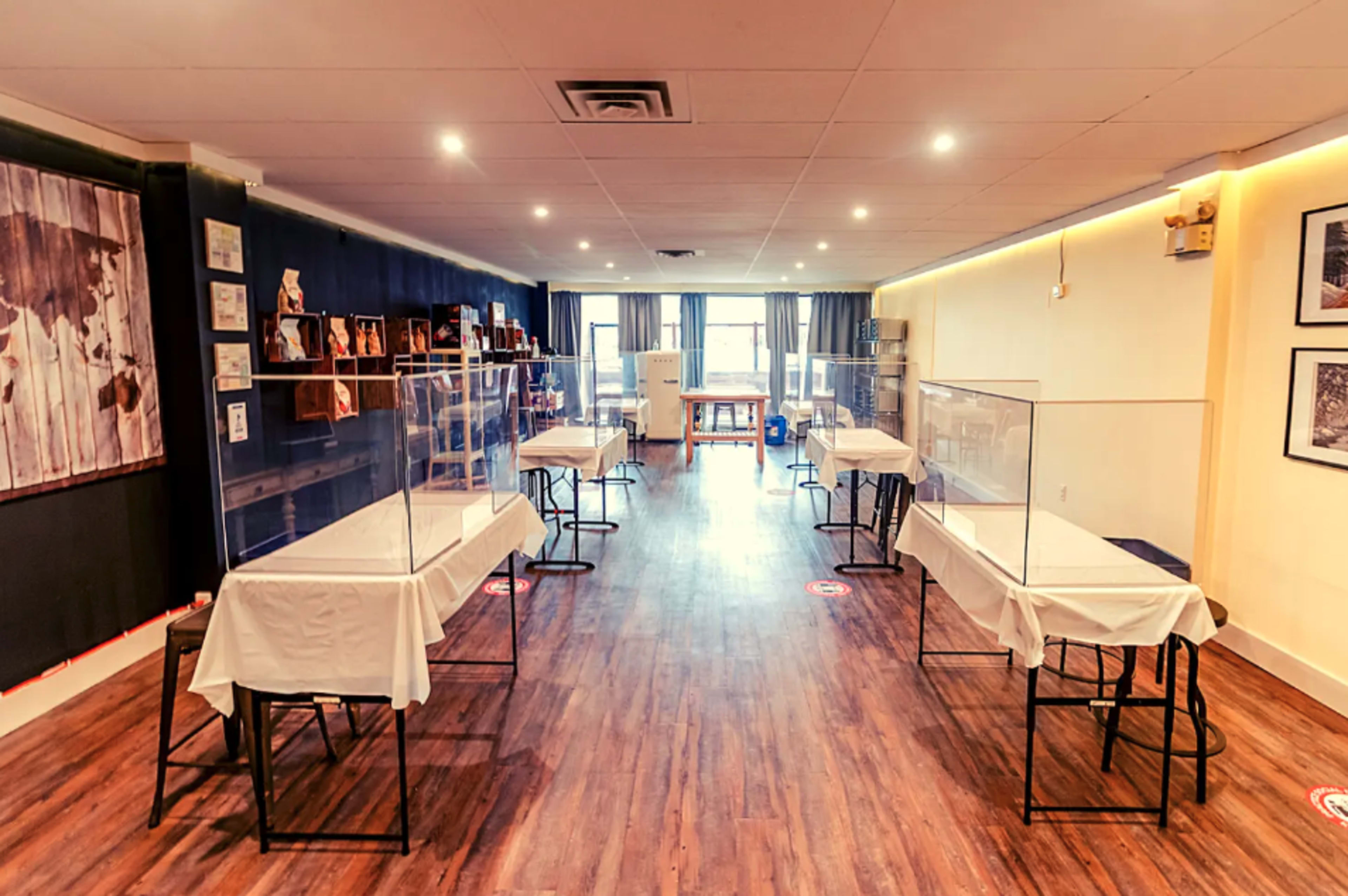 A spacious room with several tables covered in white cloth, each enclosed by clear plastic barriers, creating separate workstations.