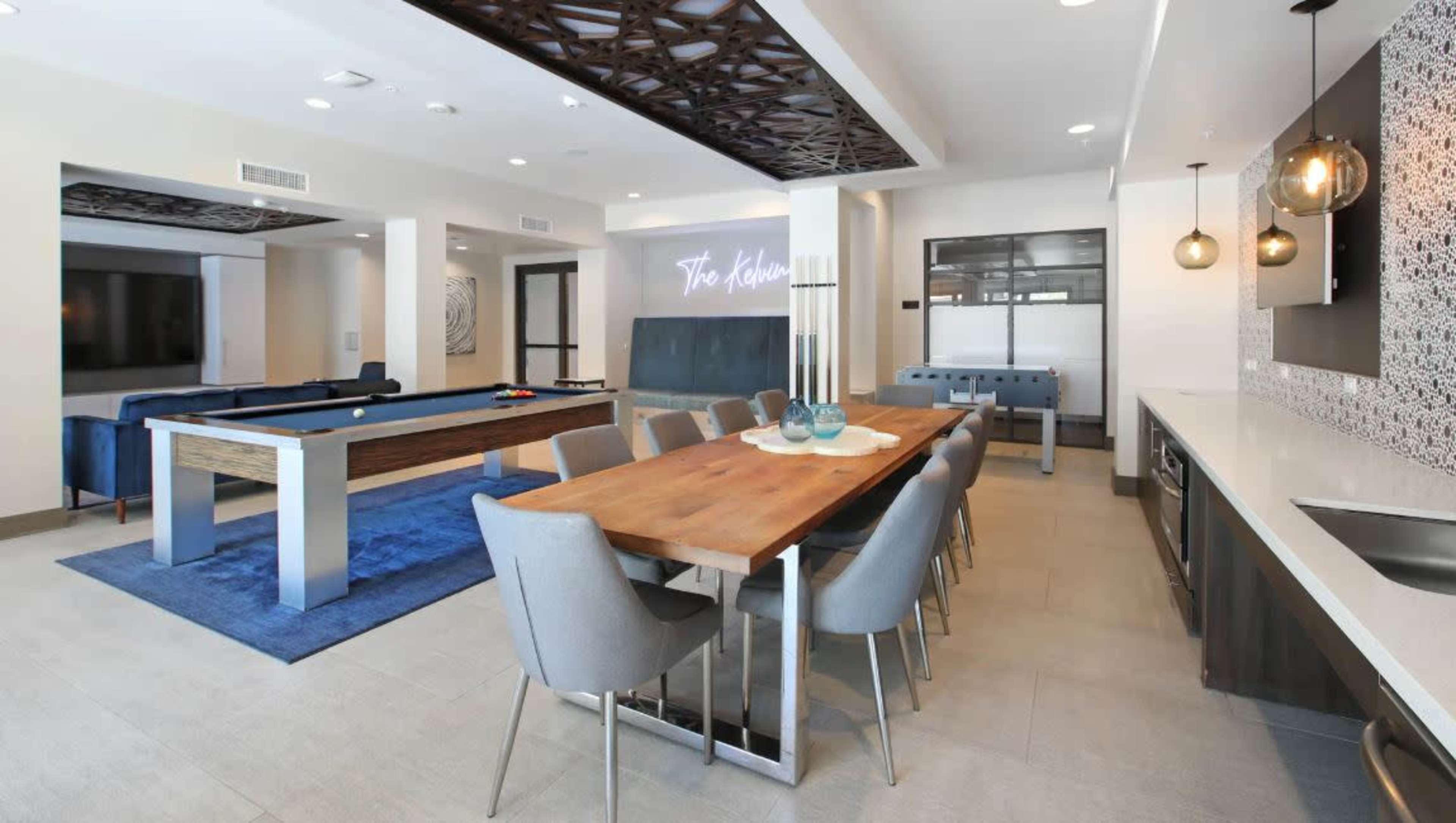 A modern communal space featuring a dining table, pool table, and a living area with couches and a television.