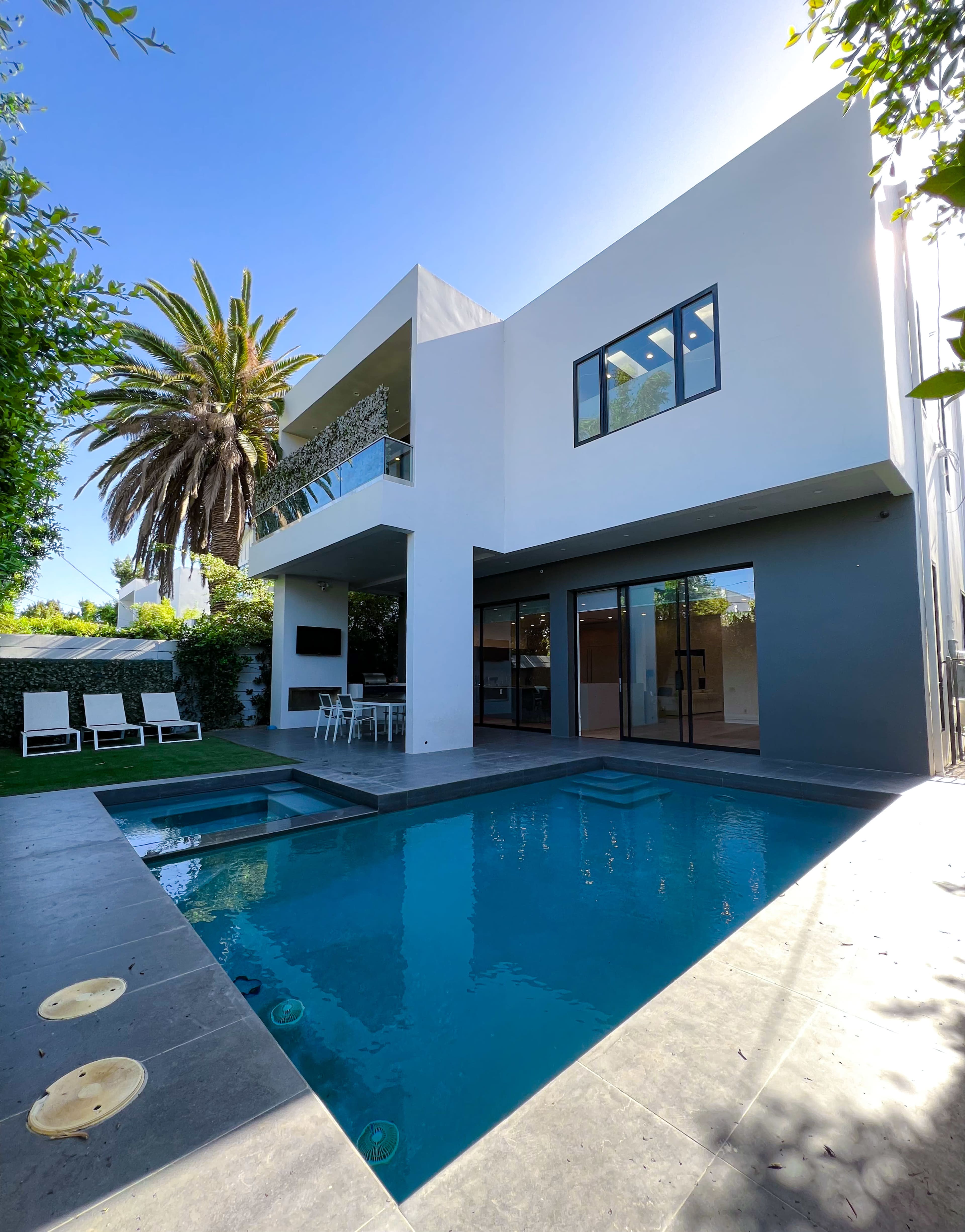 The image shows a modern two-story house with a swimming pool and a palm tree in the backyard.