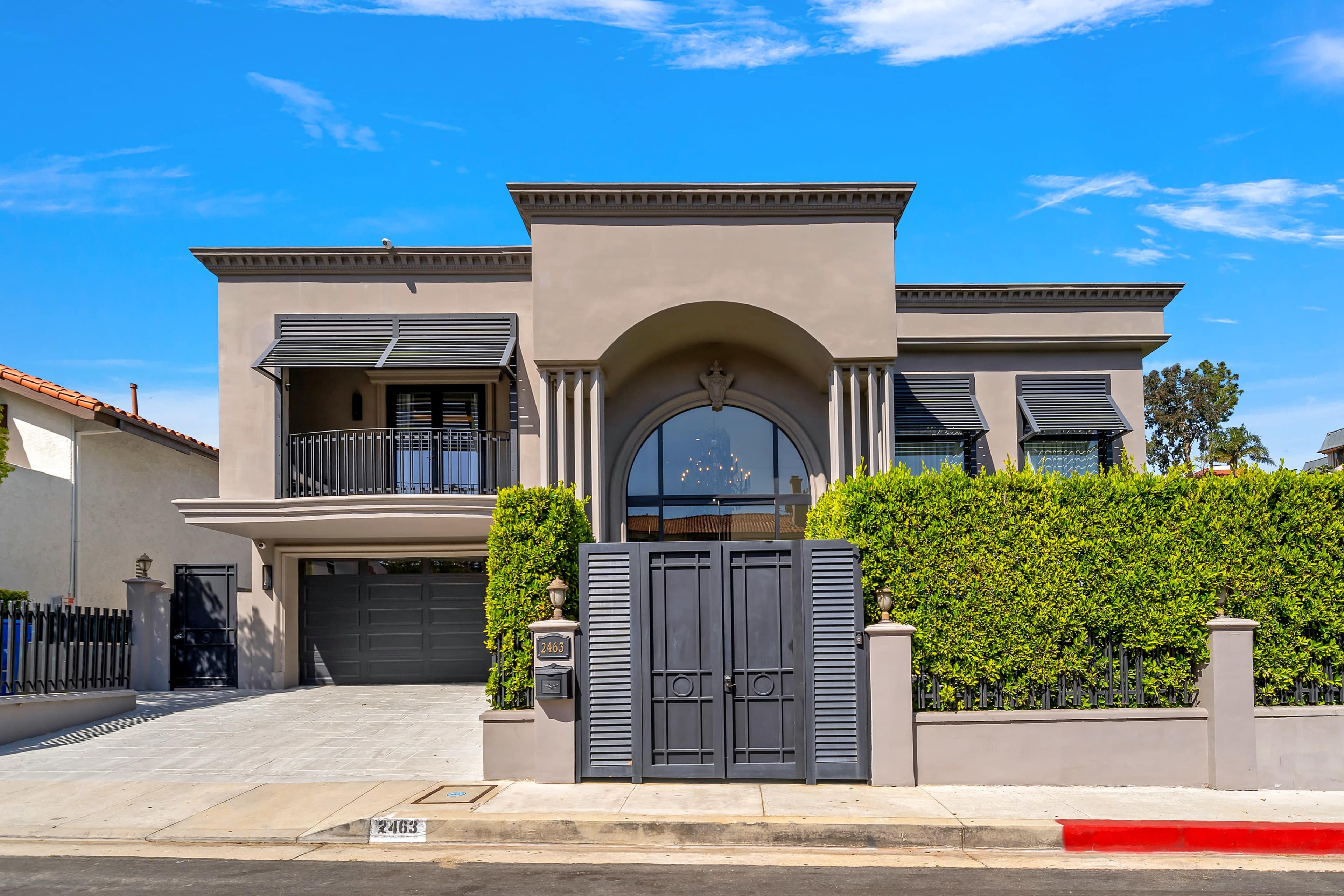 A modern, two-story house with a landscaped front yard and a large entrance gate.