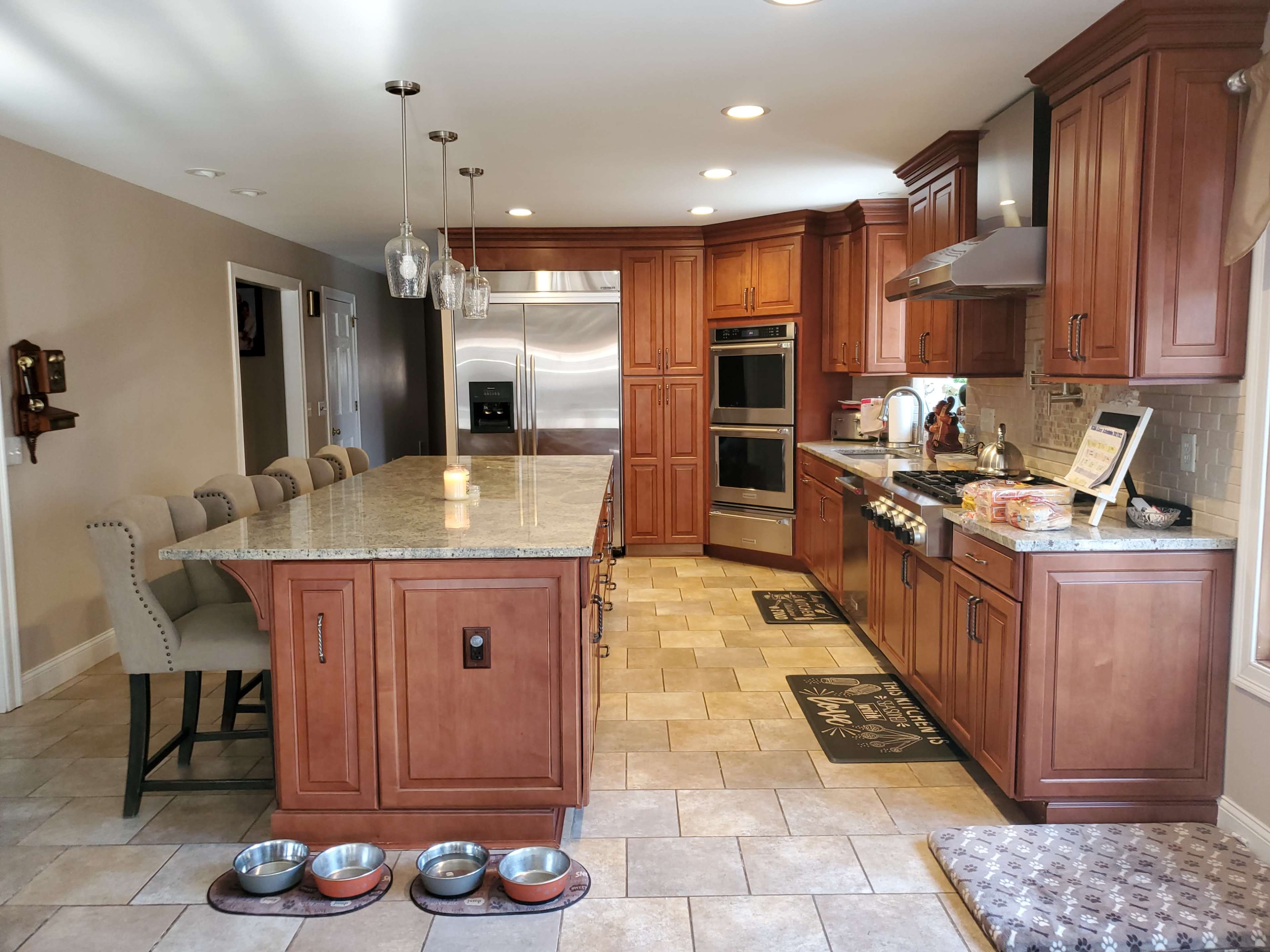 A spacious kitchen featuring wooden cabinets, a large island with seating, stainless steel appliances, and tiled flooring.