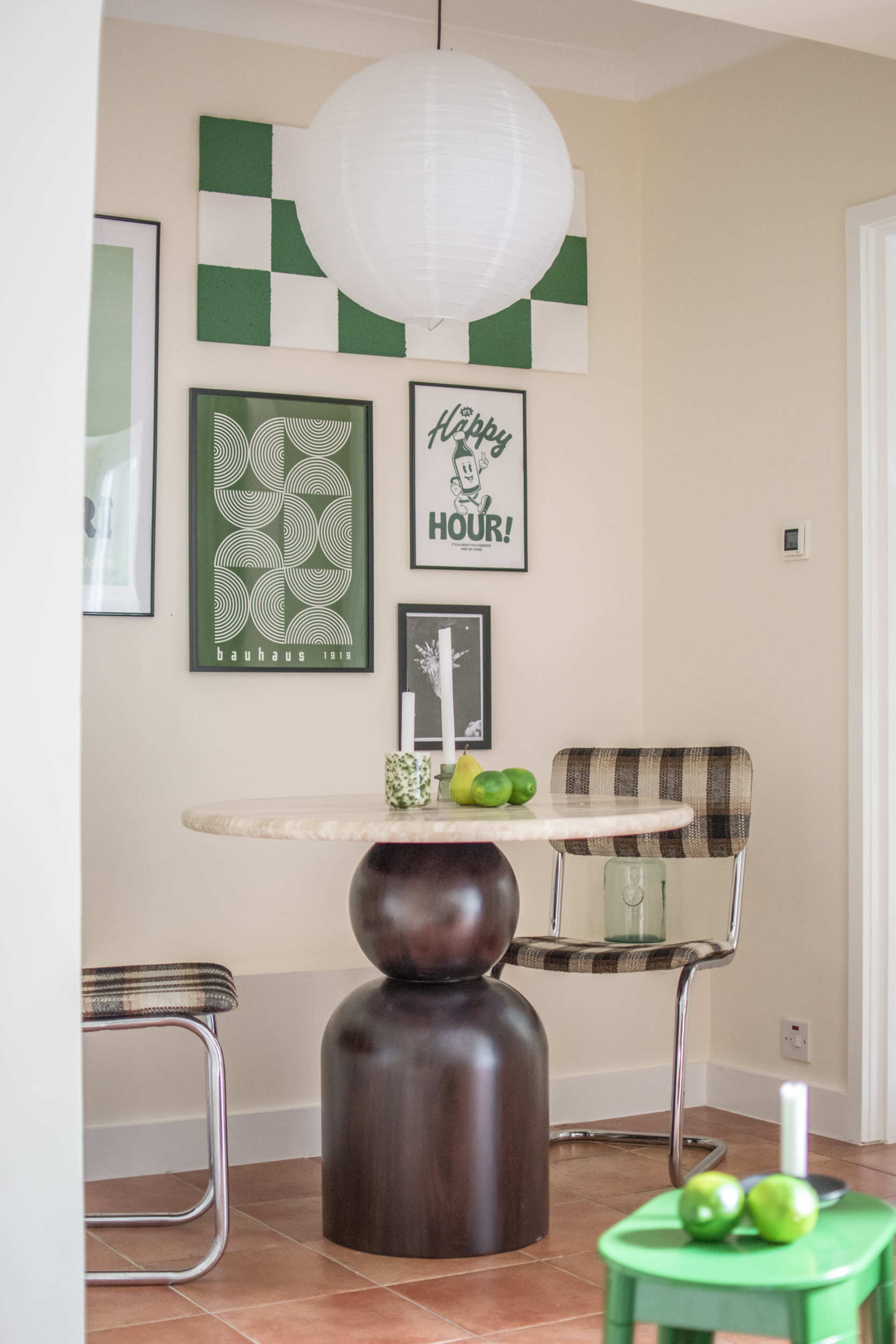 A modern dining area features a round table with a dark pedestal base surrounded by checkered chairs, adorned with framed green artwork on the wall.