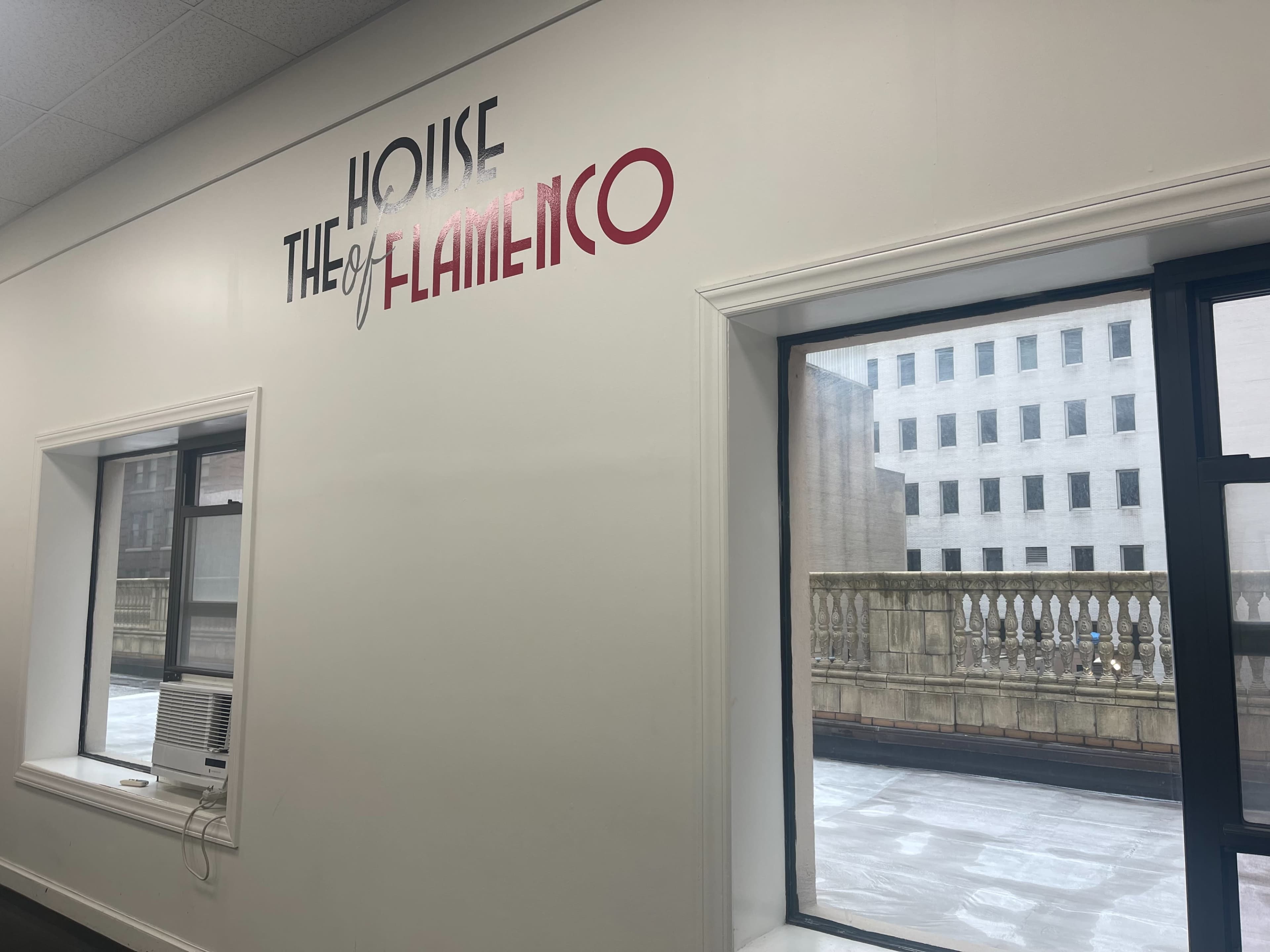 The image shows an interior wall with the text "THE HOUSE of FLAMENCO" displayed above two windows overlooking a balcony.