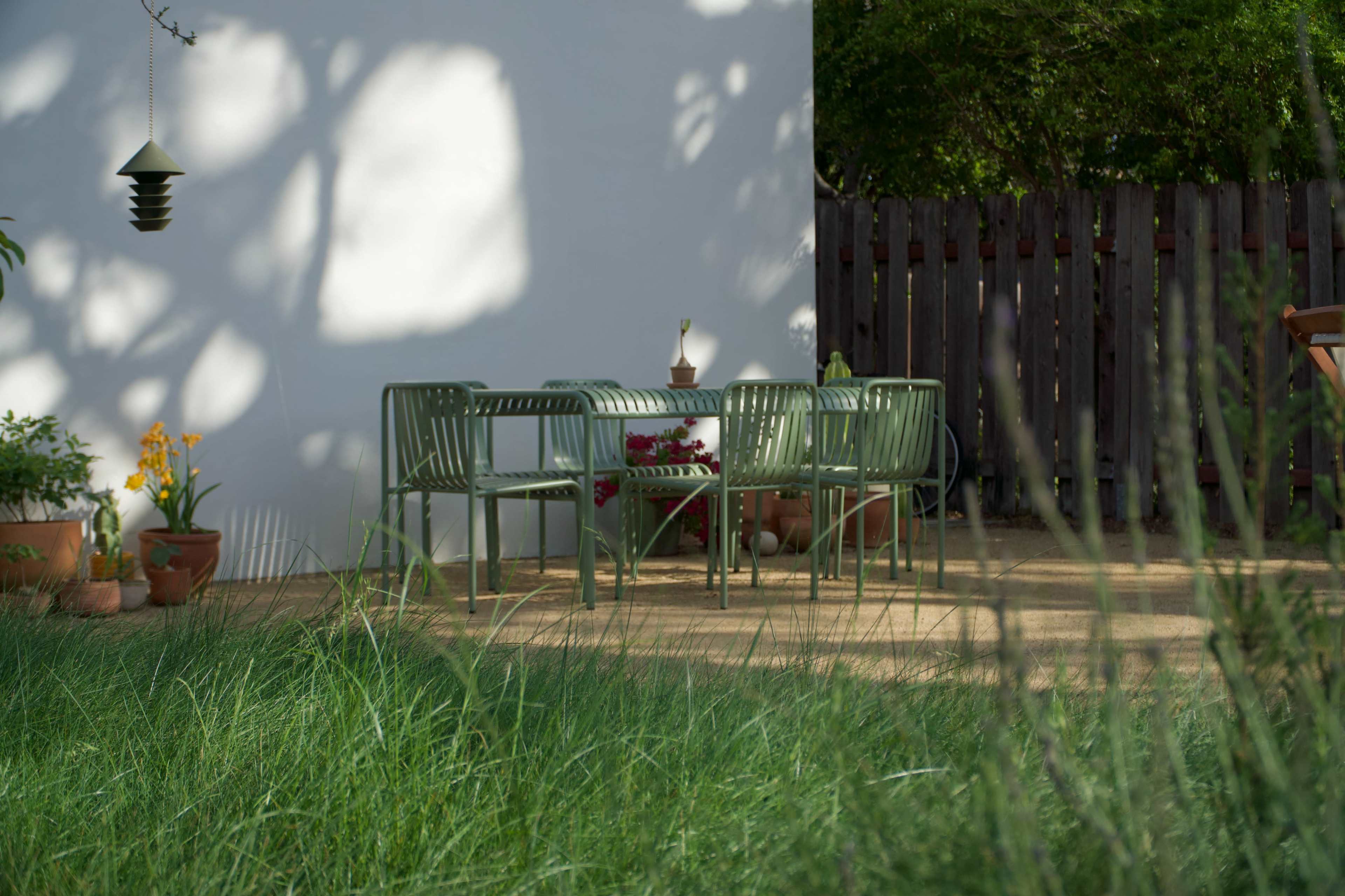 A green outdoor dining set is arranged on a patio surrounded by plants and a wooden fence.