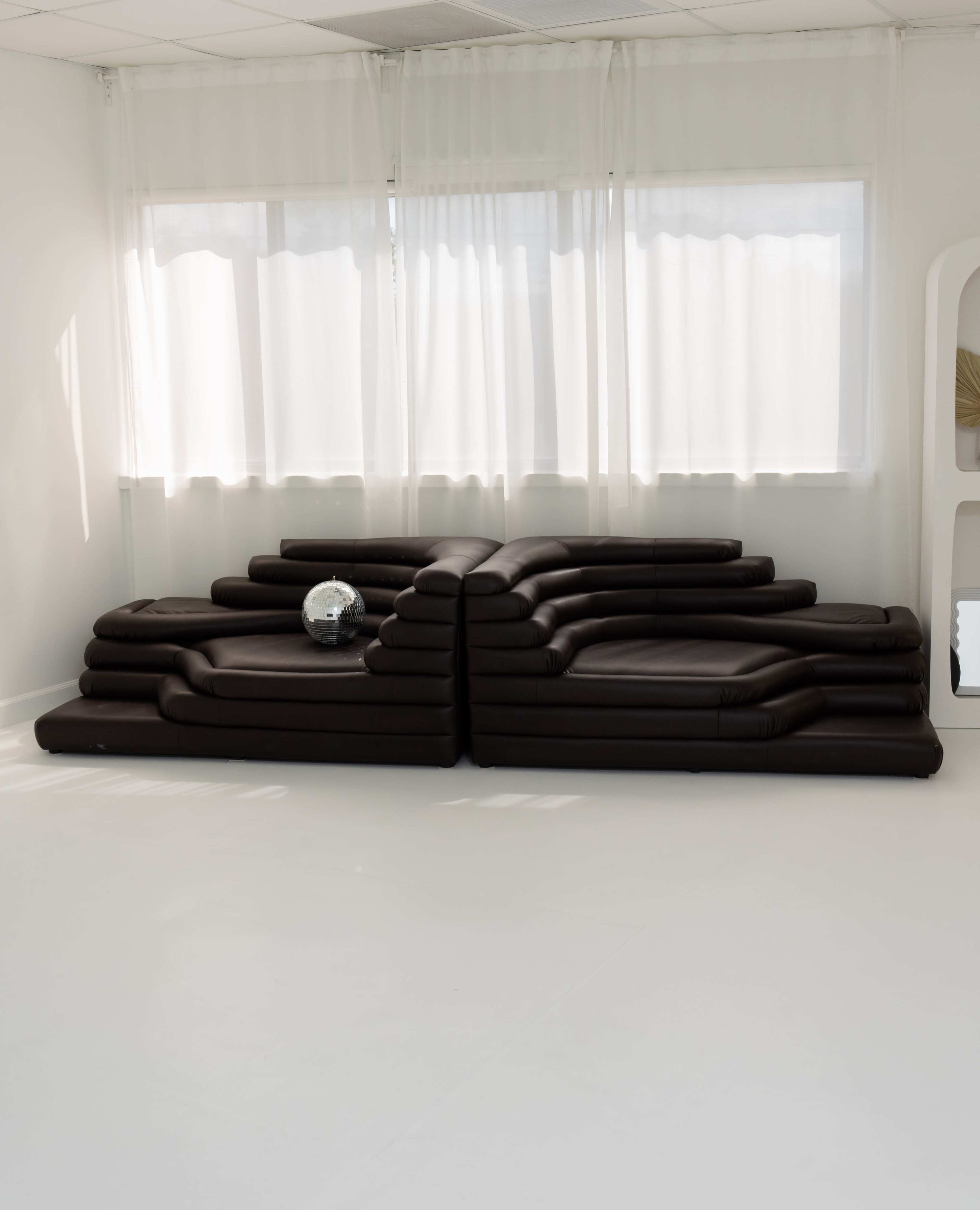 The image shows a modern, minimalist lounge area with a unique, sculptural sofa arrangement and a decorative glass ball on a side table.