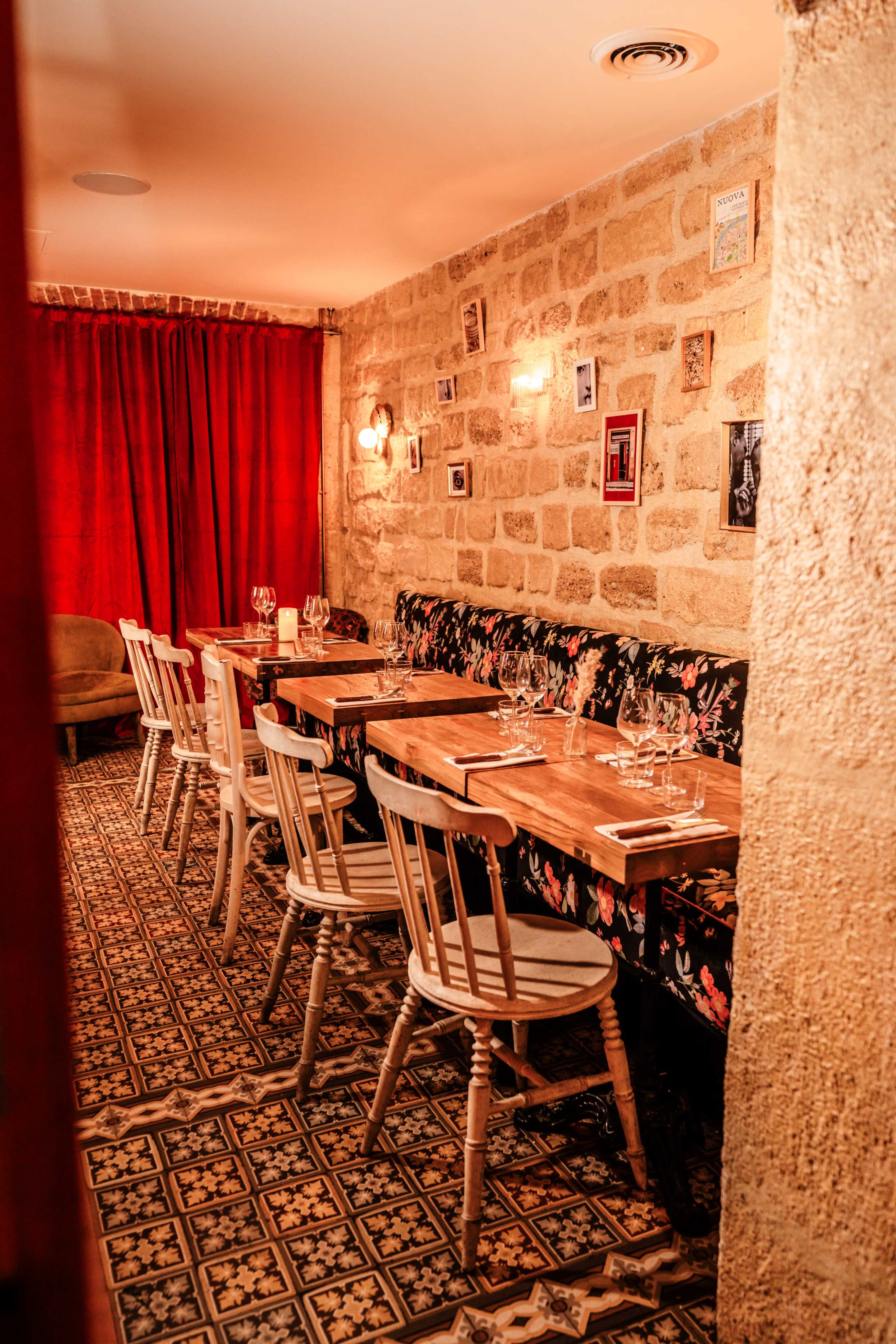 A cozy dining area with wooden tables, floral upholstered seating, and a stone wall adorned with framed photos.